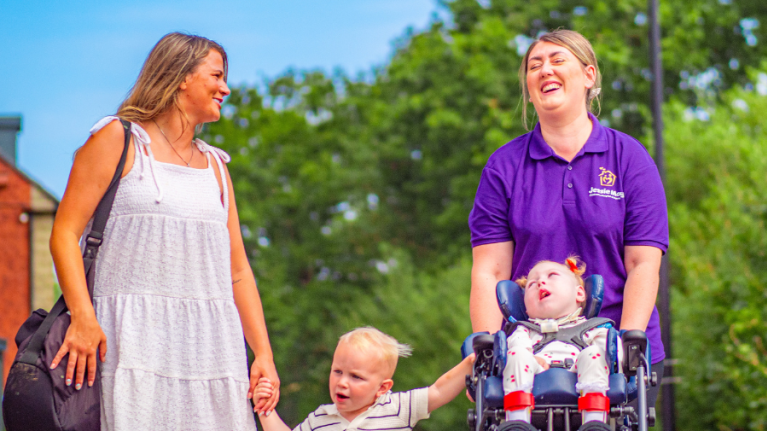 A mum, son, daughter and their carer takes a walk together. They are laughing and smiling.