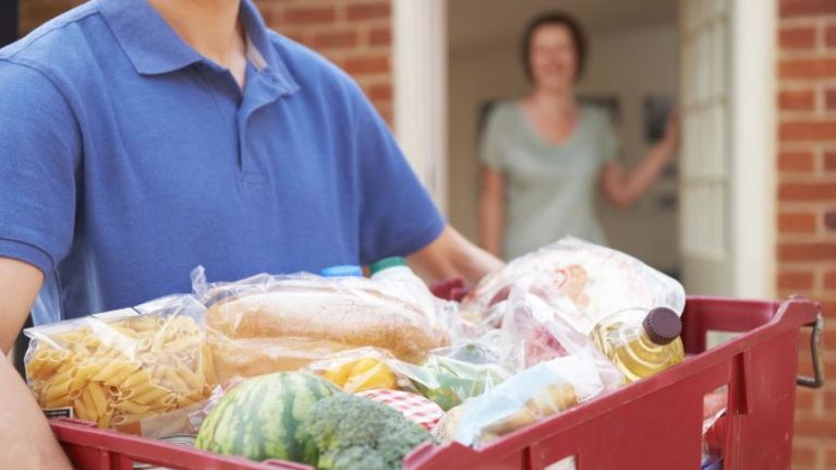 Man in blue t-shirt holding a box of food at someone's front door