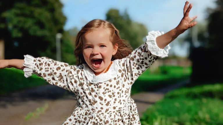 A little girl is smiling joyfully at the camera in the garden