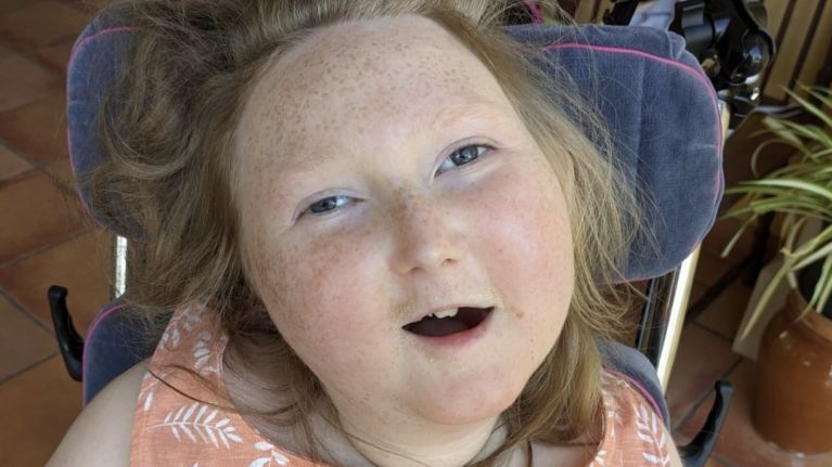 A young girl in a wheelchair is smiling up at the camera