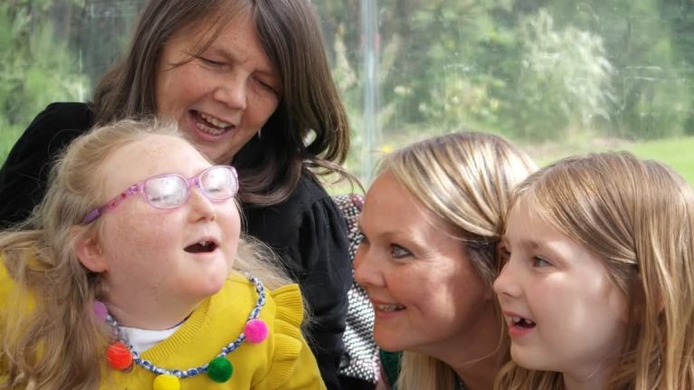 A family of two women and a young girl are smiling at another family member, a young girl
