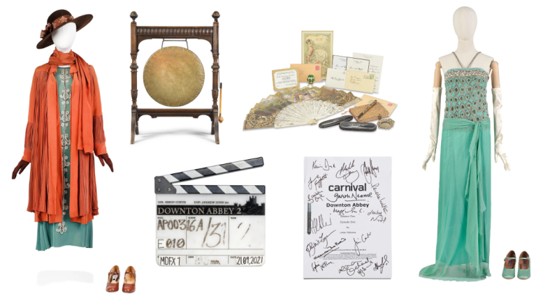 A collection of costumes and props from Donwton Abbey. Includes a brass gong, a film clapper prop labelled Downton Abbey, a signed script and two female costumes