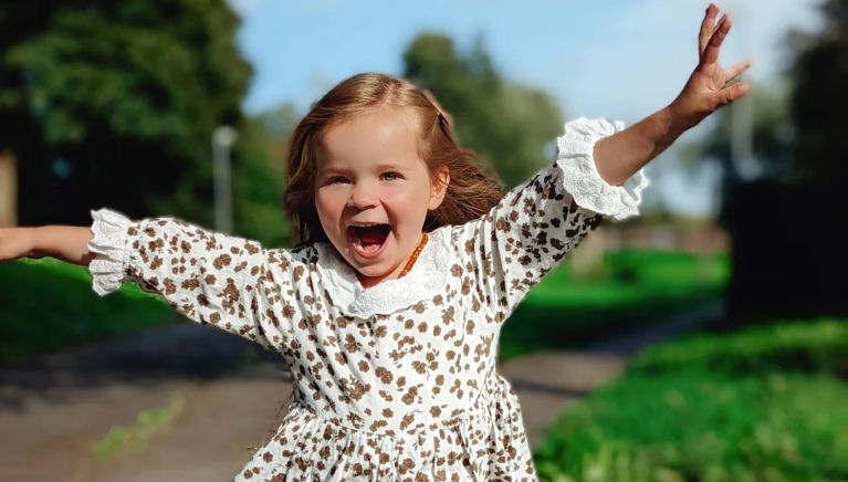 A little girl is smiling joyfully at the camera in the garden