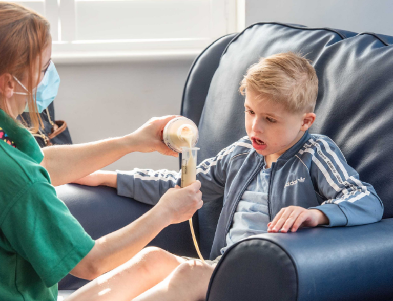 Nurse giving feed to little boy at children's hospice
