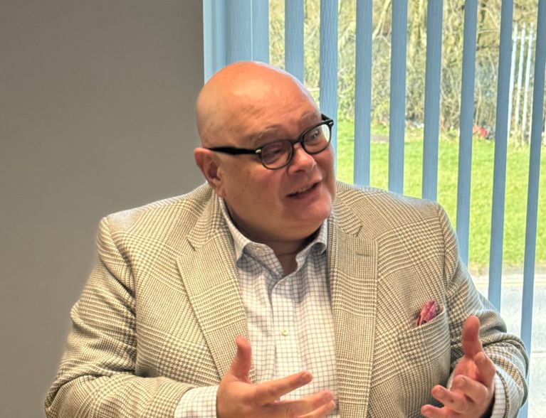 Andrew Heywood Hughes, sitting at a desk. He is gesturing with his arms as he explains something.
