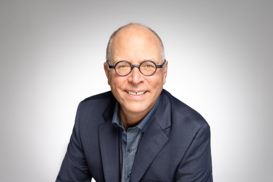 Head shot of Chad Coerver wearing a dark blue blazer and round glasses.