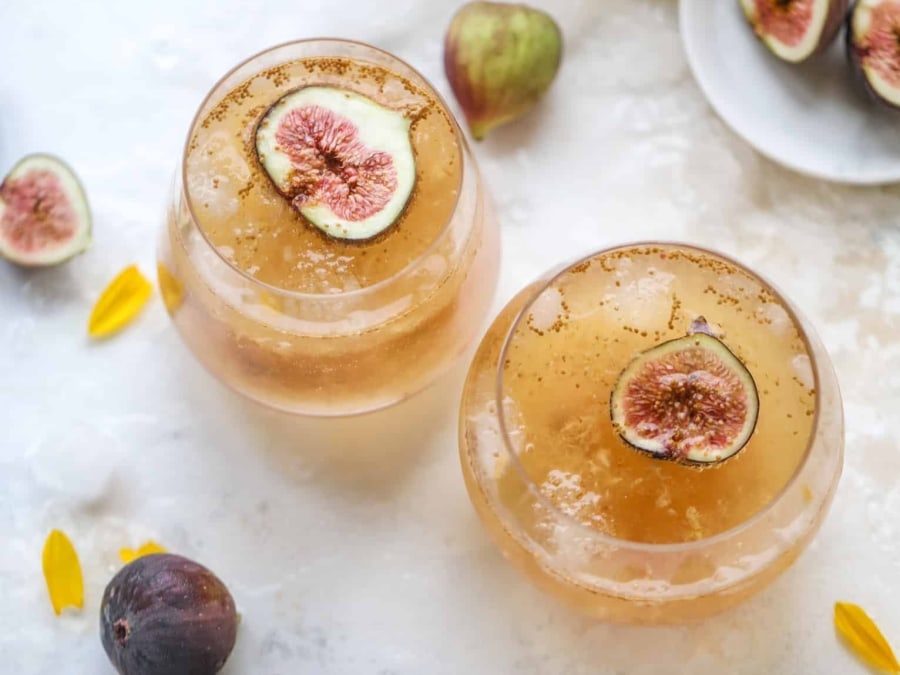Two full glasses from above, showing a gold-colored cocktail with two fig halves on top