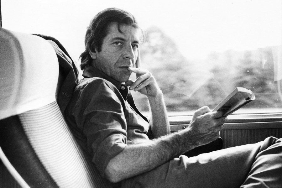 Black-and-white image of Leonard Cohen, sitting on a train and looking towards the camera 