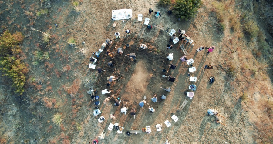 An aerial photo of a circle of people digging a large dirt hole.