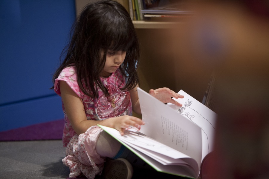 A young girl with dark hair reads a picture book.