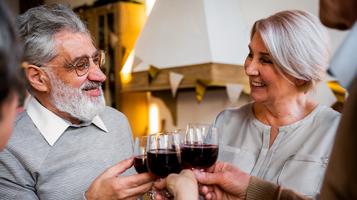 Senior couple toasting with wine glasses alongside friends, celebrating a wedding anniversary and special milestone together