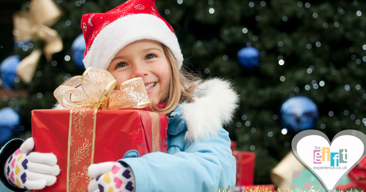 Little girl in a Santa hat holding a gift by the Christmas Tree Little girl in a Santa hat holding a gift by the Christmas Tree