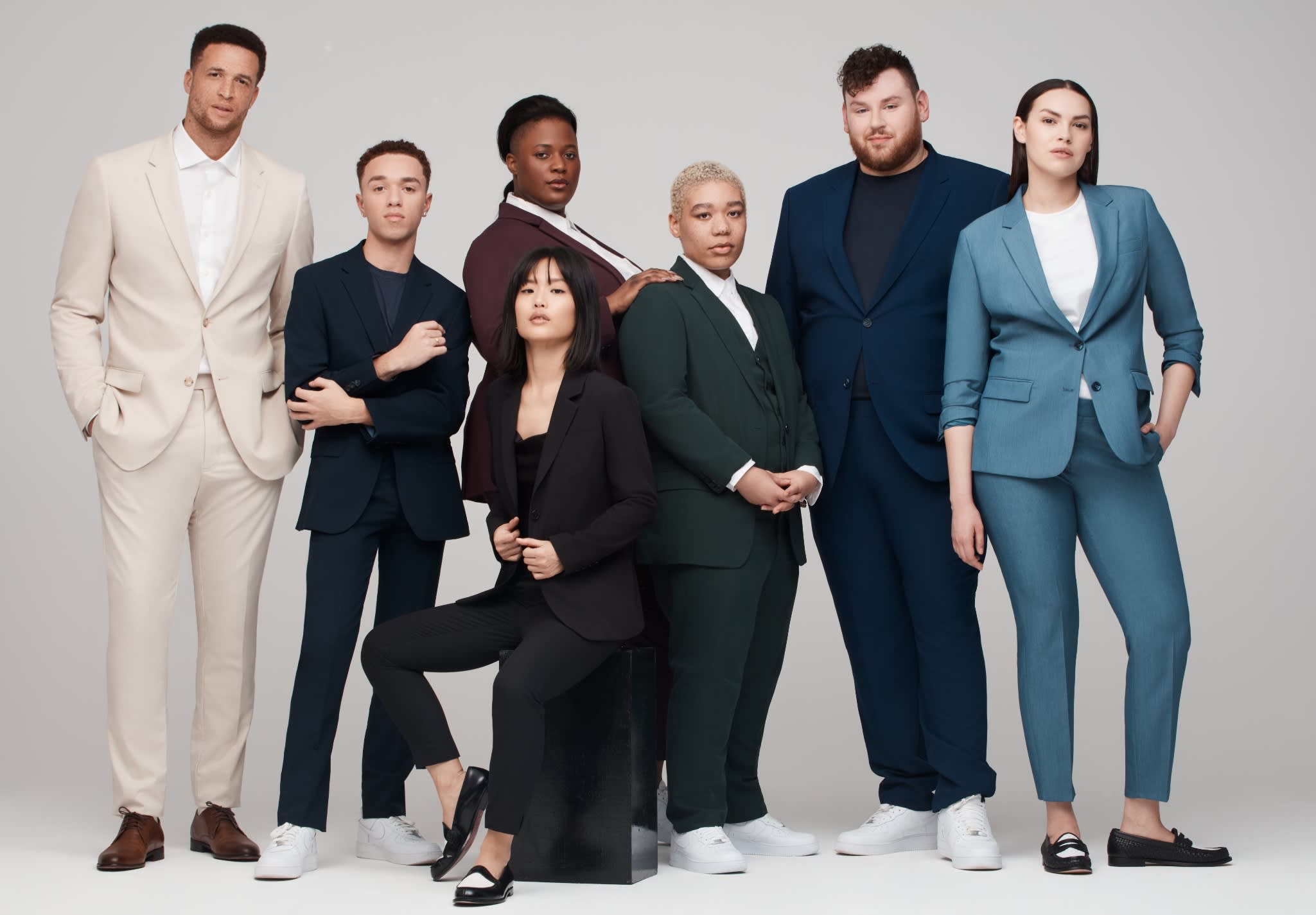 A diverse group of men, women, and non-binary individuals in many different colored suits, showcasing SuitShop's wholesale offerings.