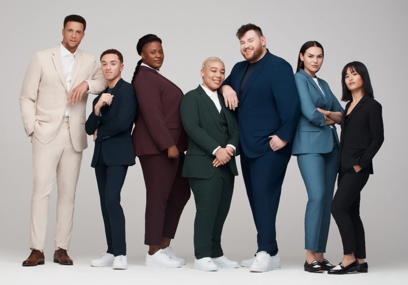 A diverse group of men, women, and non-binary individuals in many different colored suits and tuxedos, showcasing SuitShop colors and fabrics.