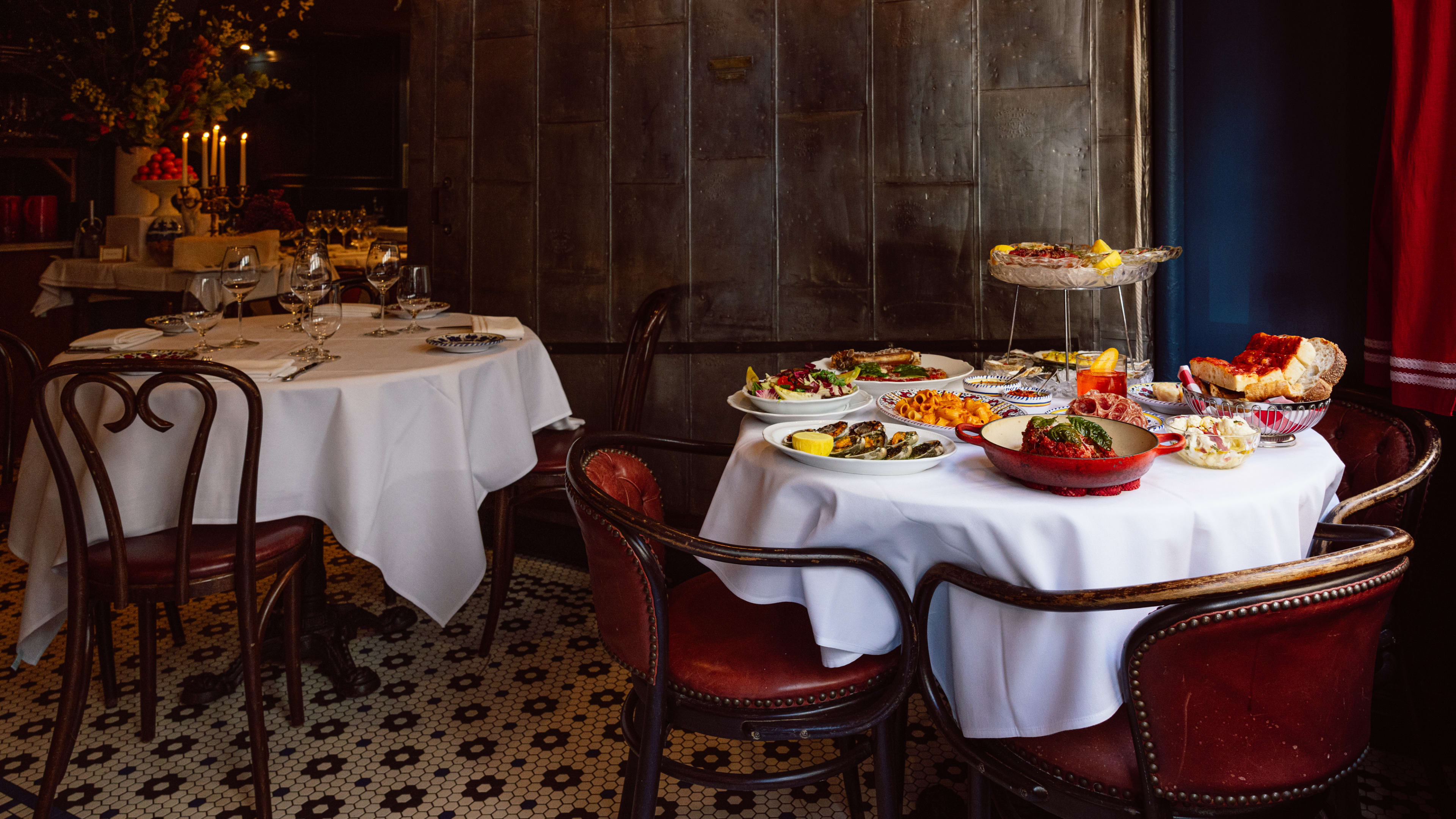 A spread of dishes from Carbone on a table with a white tablecloth with red chairs.