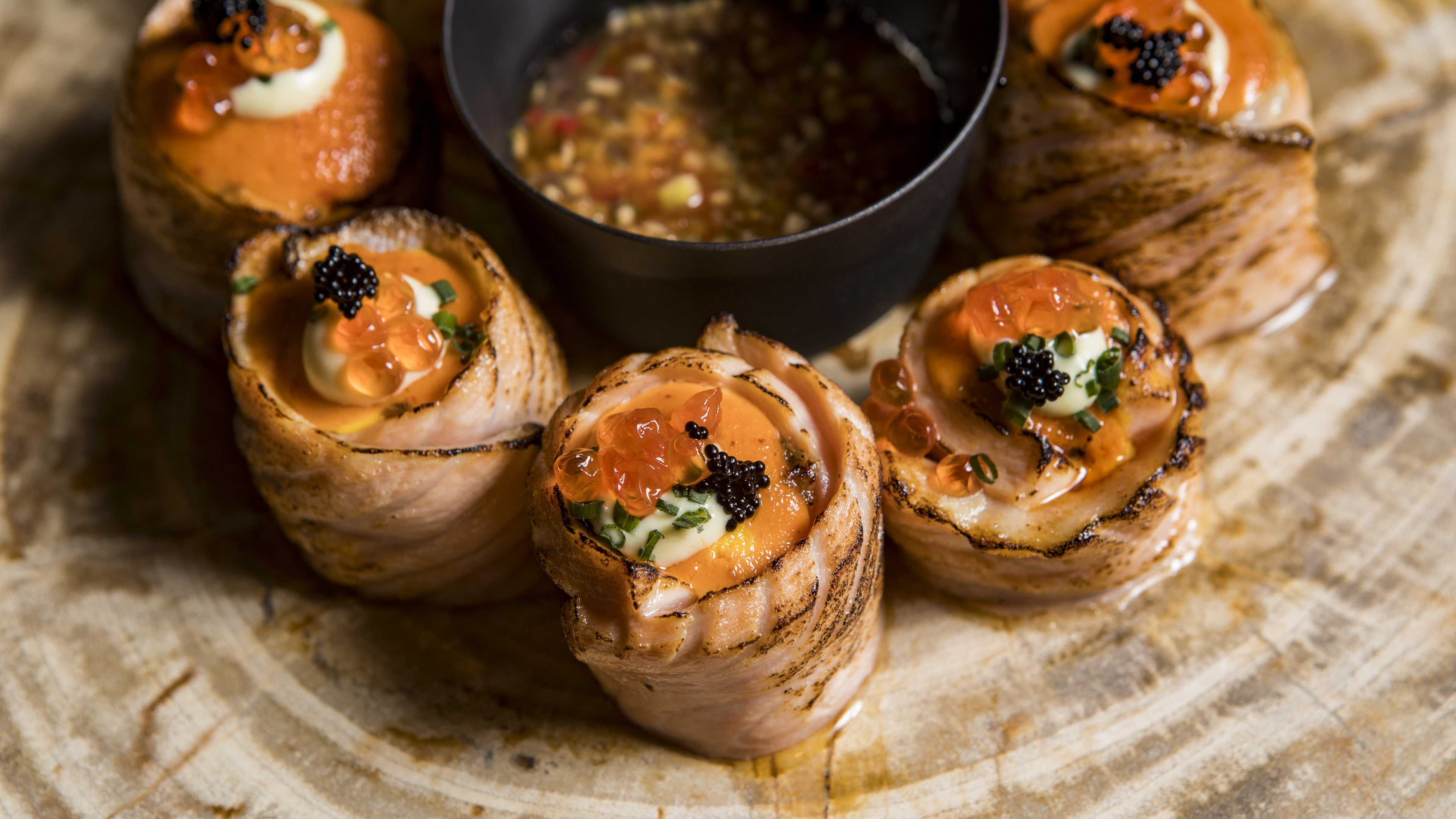 Salmon rolls topped with tobiko and caviar stacked around a bowl of dip