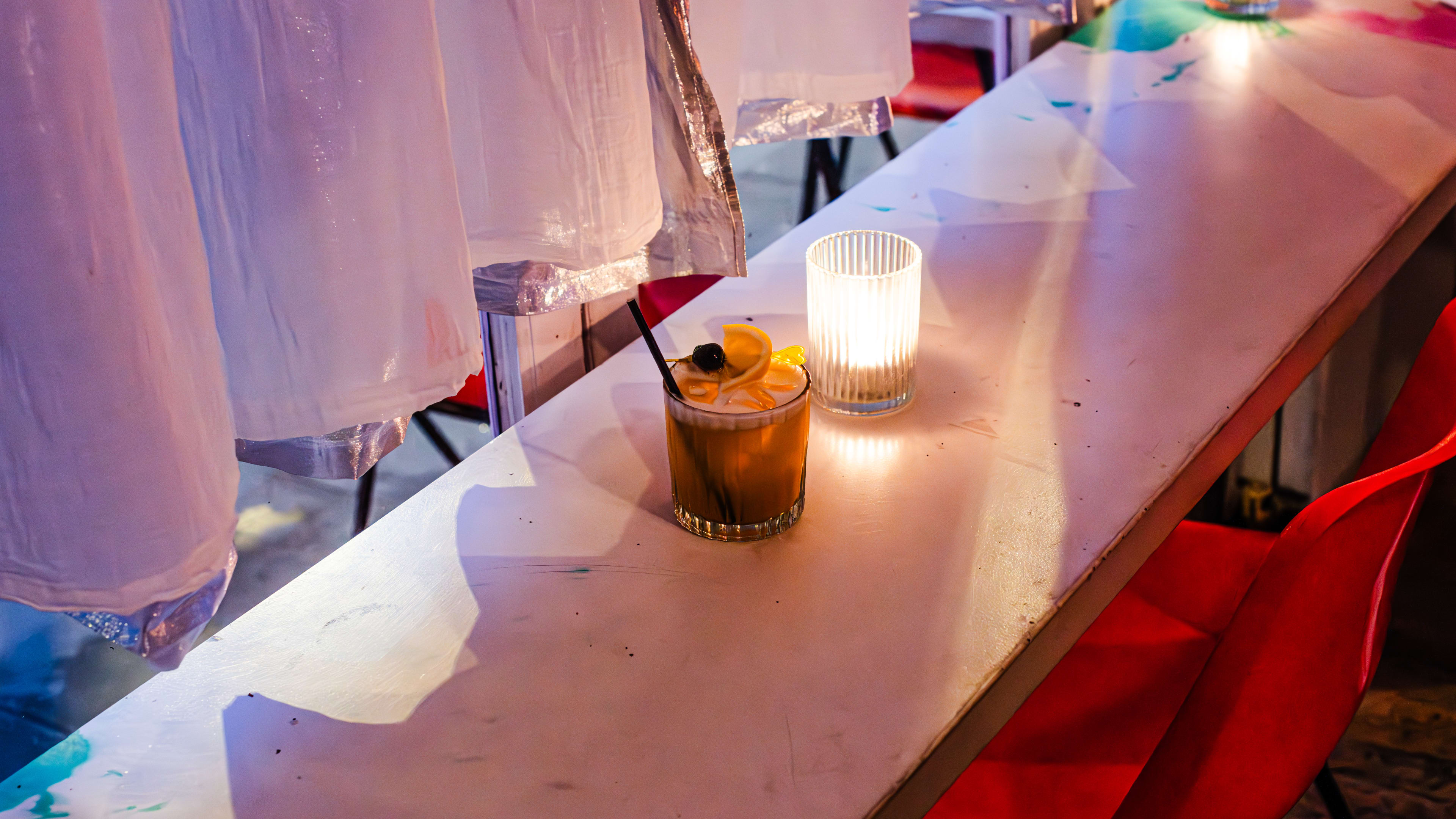 A whiskey sour cocktail on a window table of a cafe/bar at night.