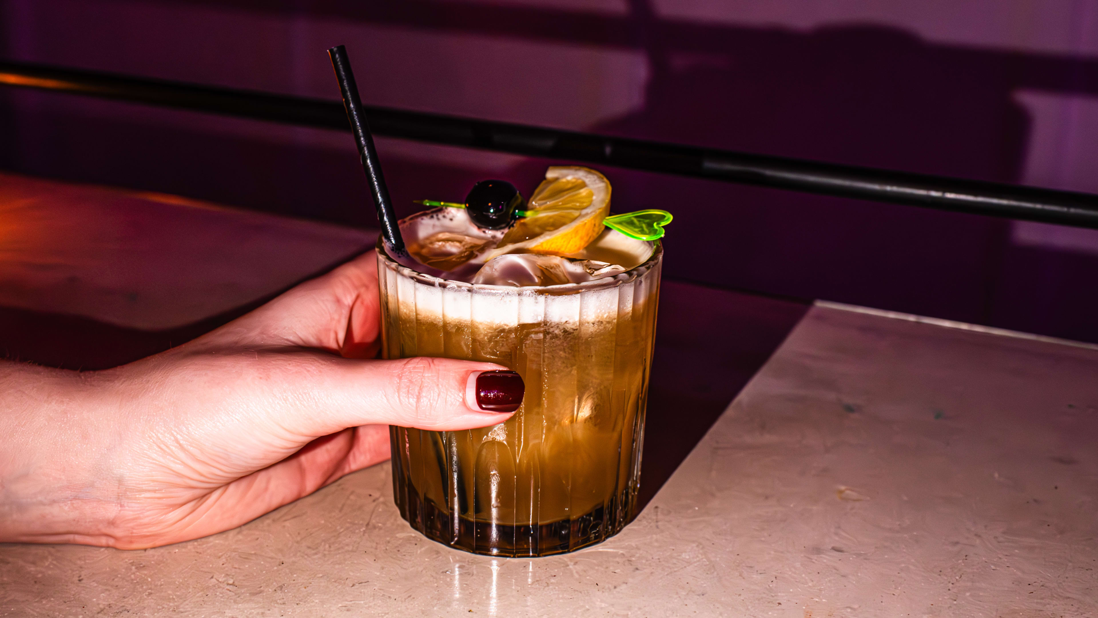 A hand with red nails holding a whiskey sour cocktail.