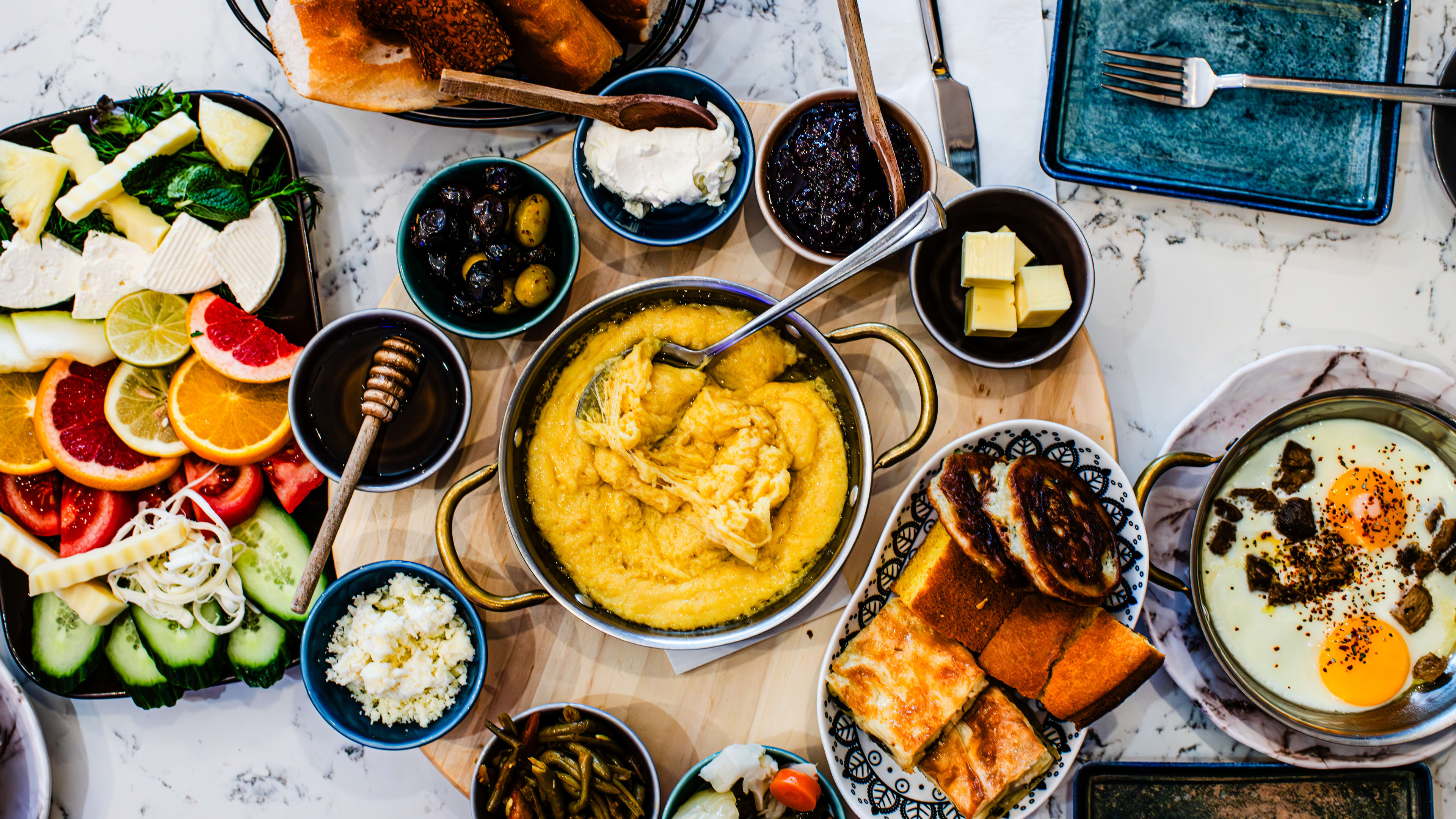 An overhead shot of the Turkish Karadeniz breakfast spread with cornmeal-thickened cheese, dips, pickles, eggs, and fruit.