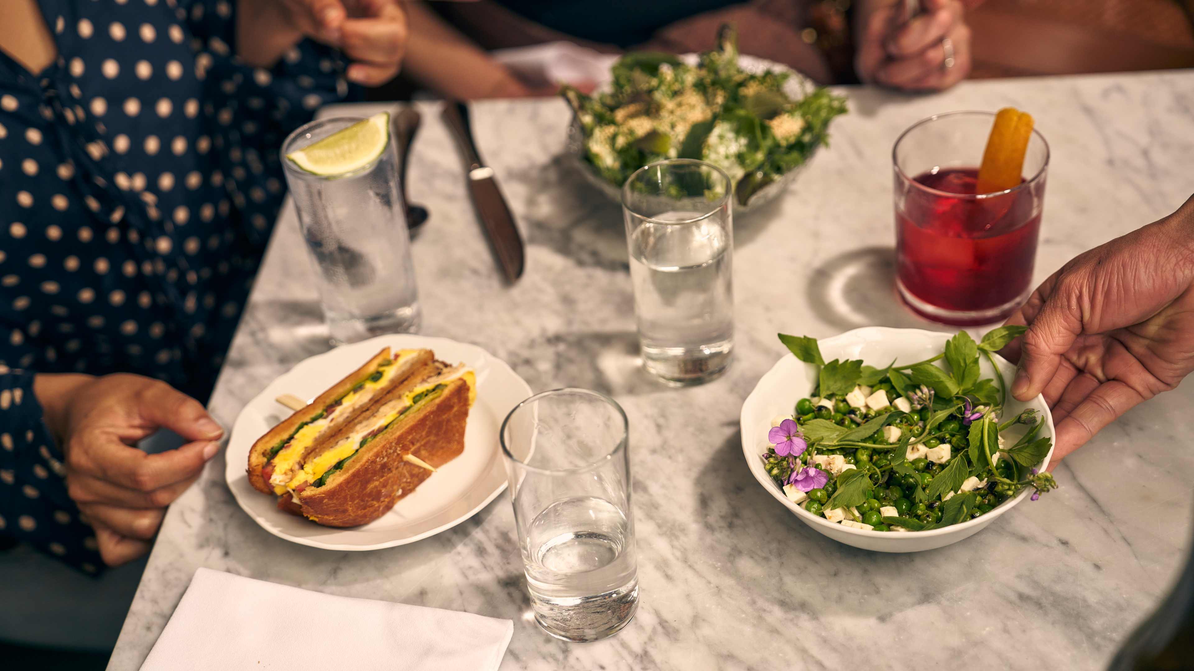 peas and sandwich on a table with people's hands reaching for food at Cafe Mado