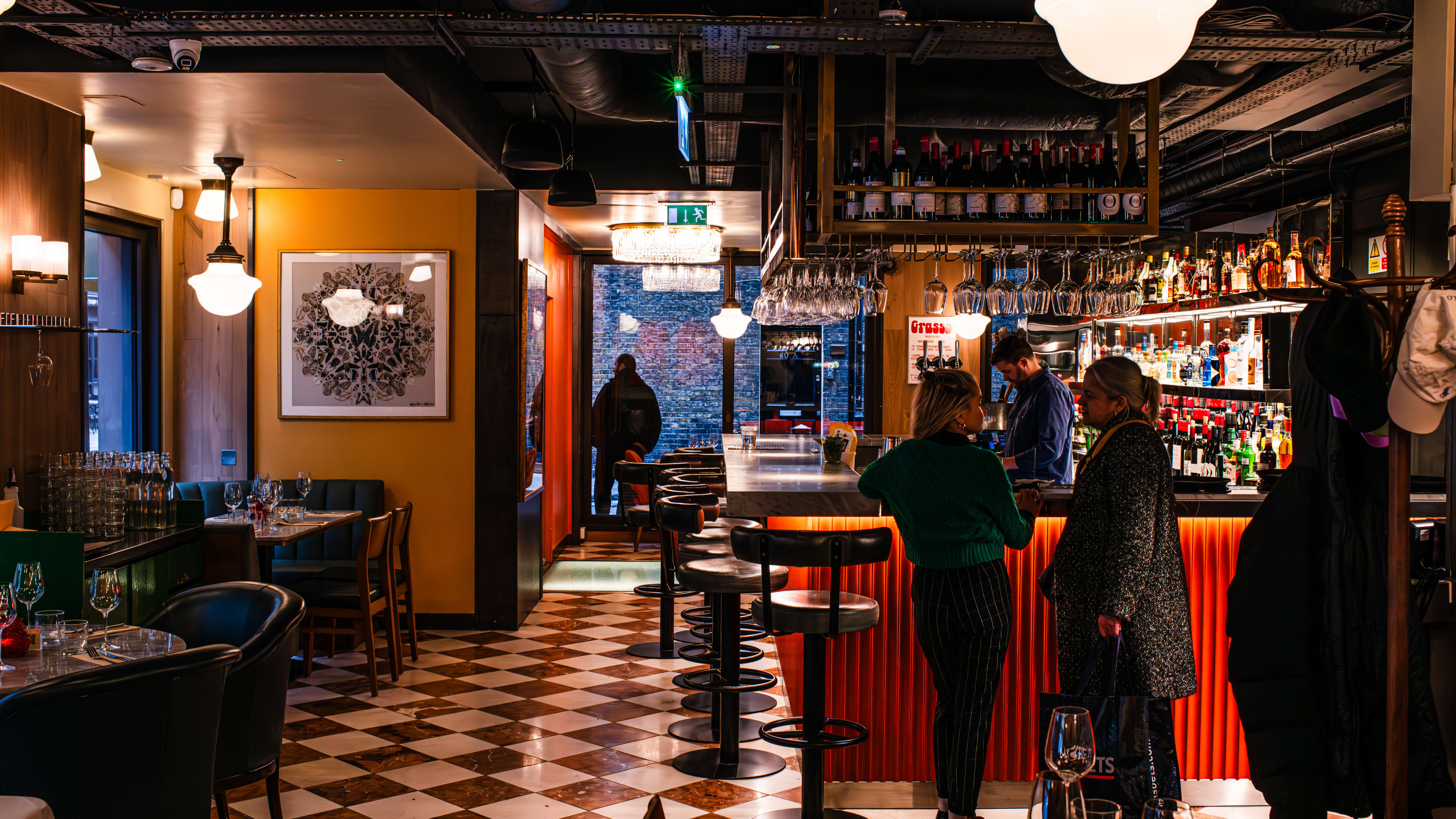 Interior of a restaurant with checkered floor tiling and bottles around a bar.