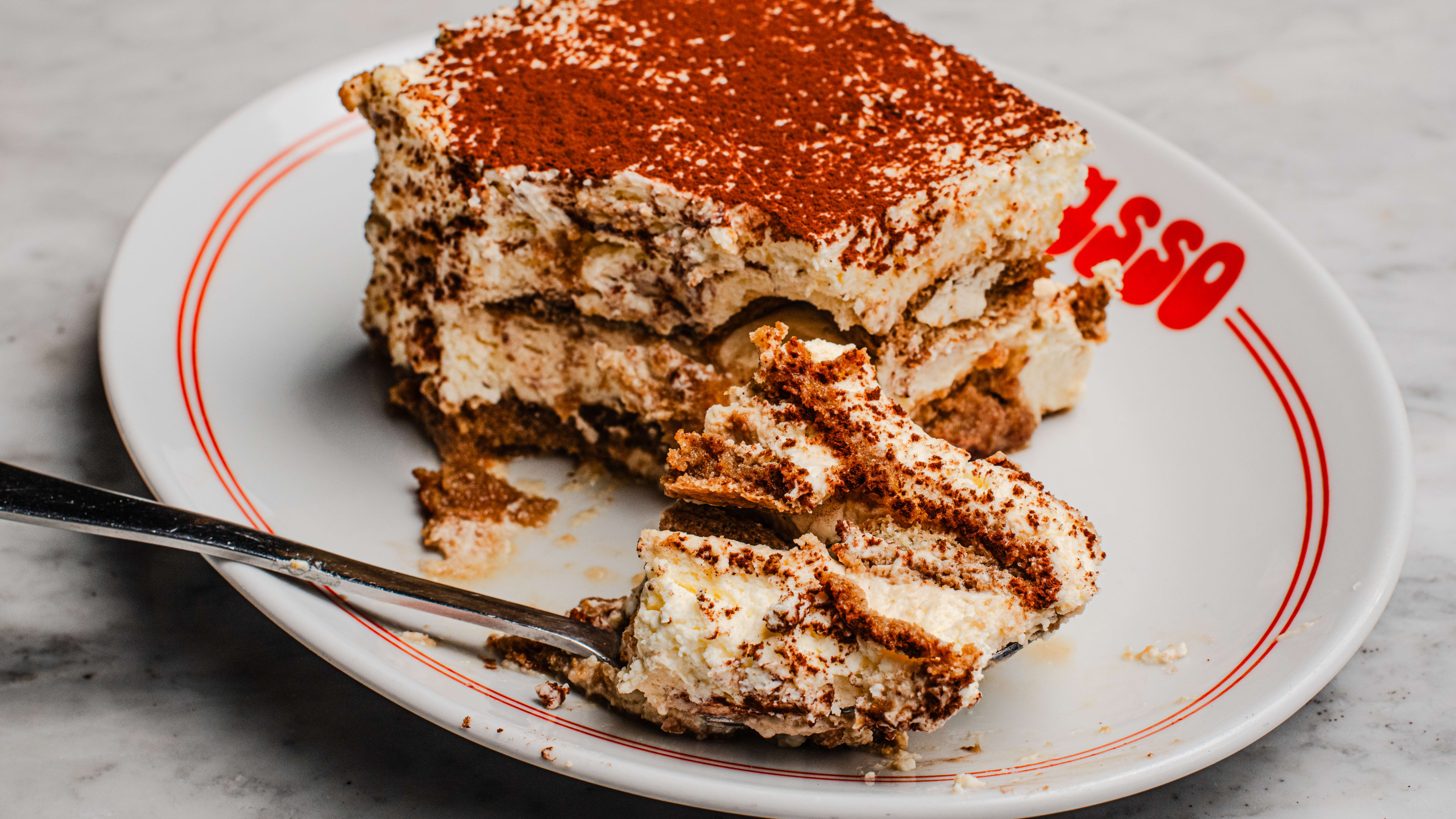 A plate of tiramisu with a spoonful taken out and shown in the foreground.