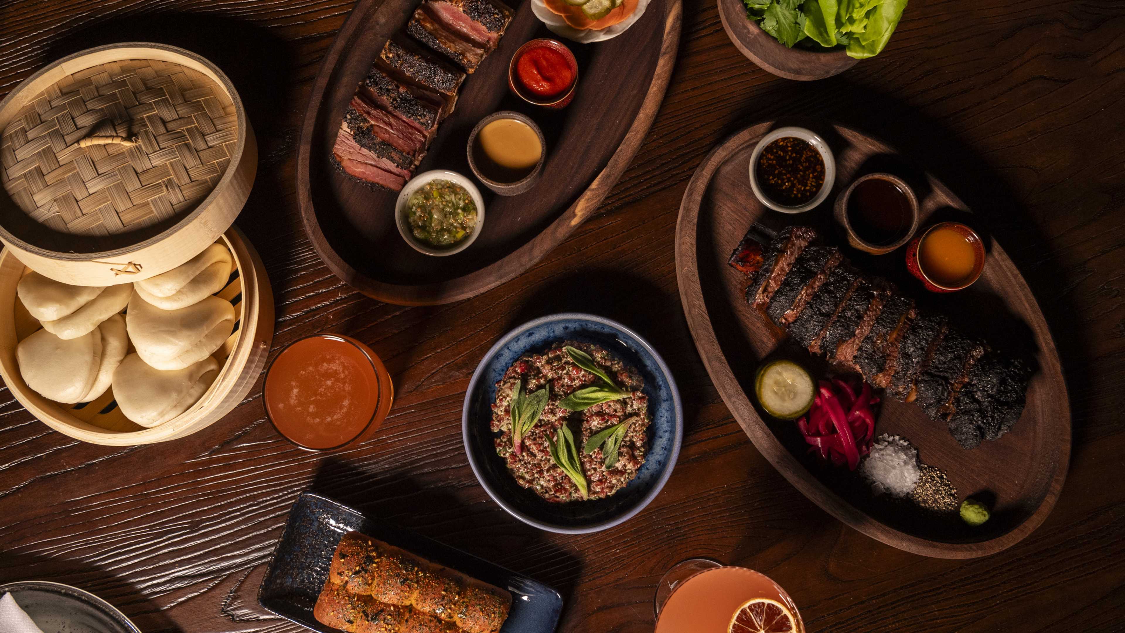 Spread of food and cocktails including bao buns, short rib, and pastrami