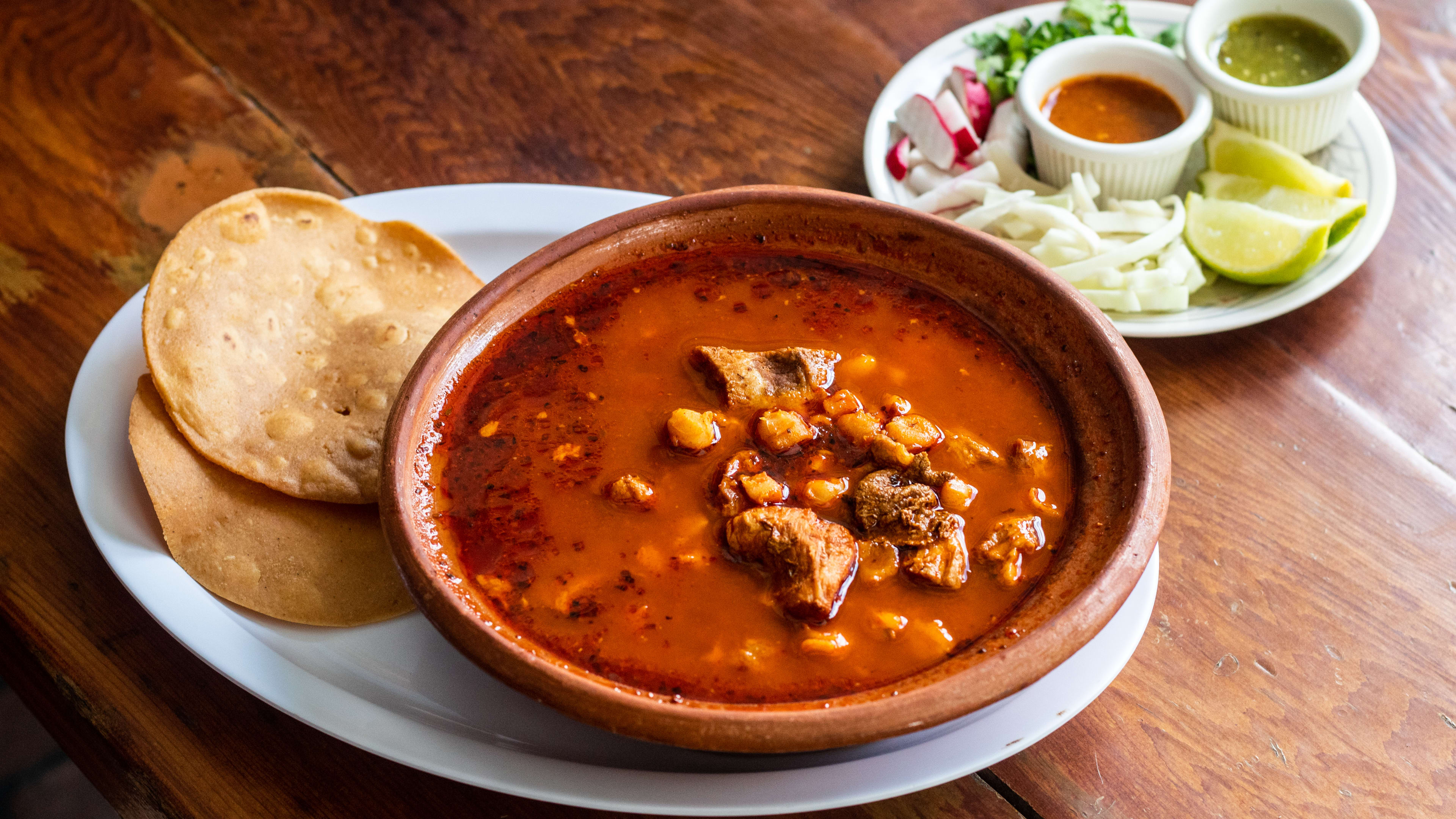 Bowl of pozole with tostadas as well as lime and sauces