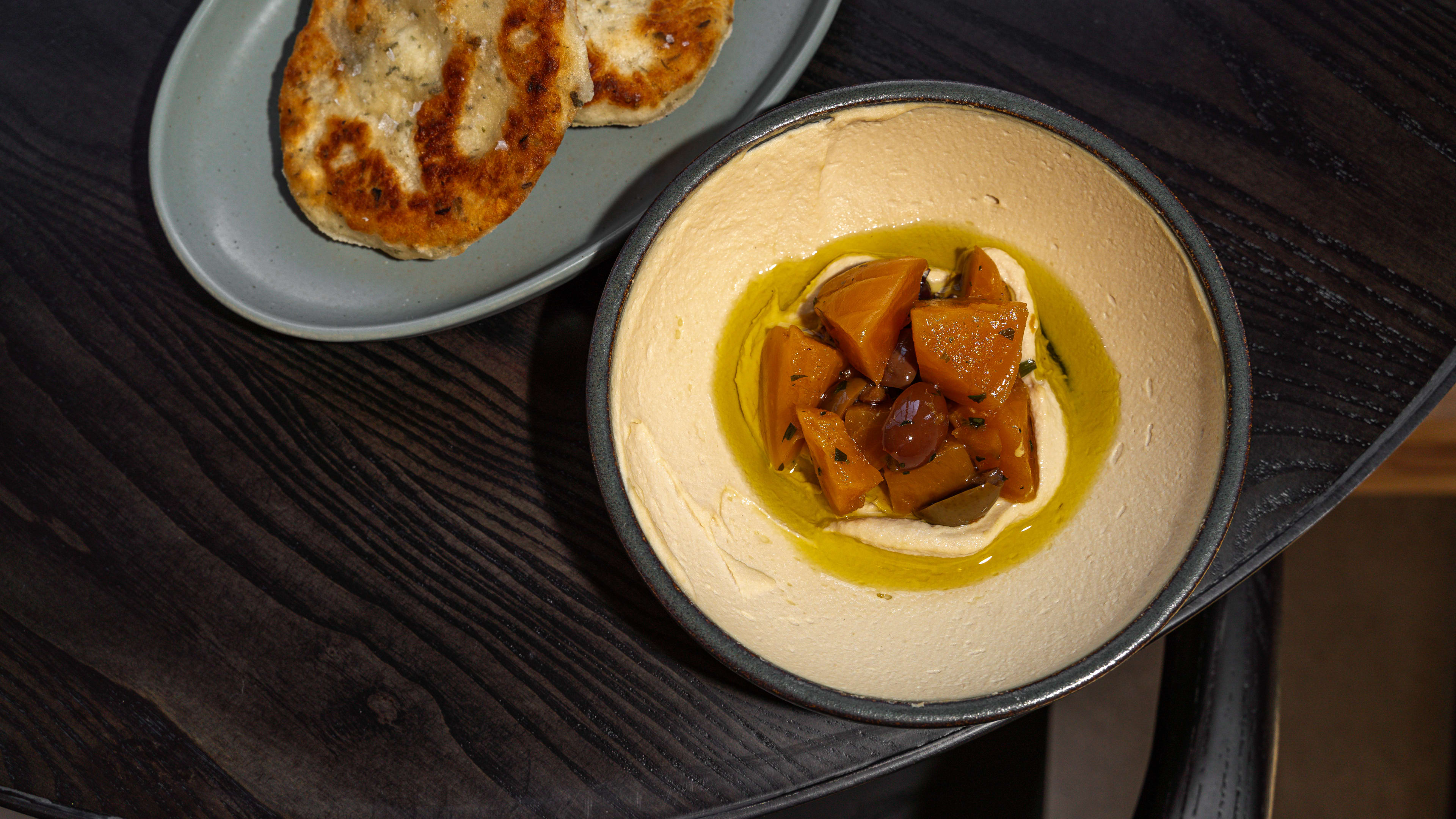 Table with a plate of griddle bread and a bowl of smooth hummus topped with beets