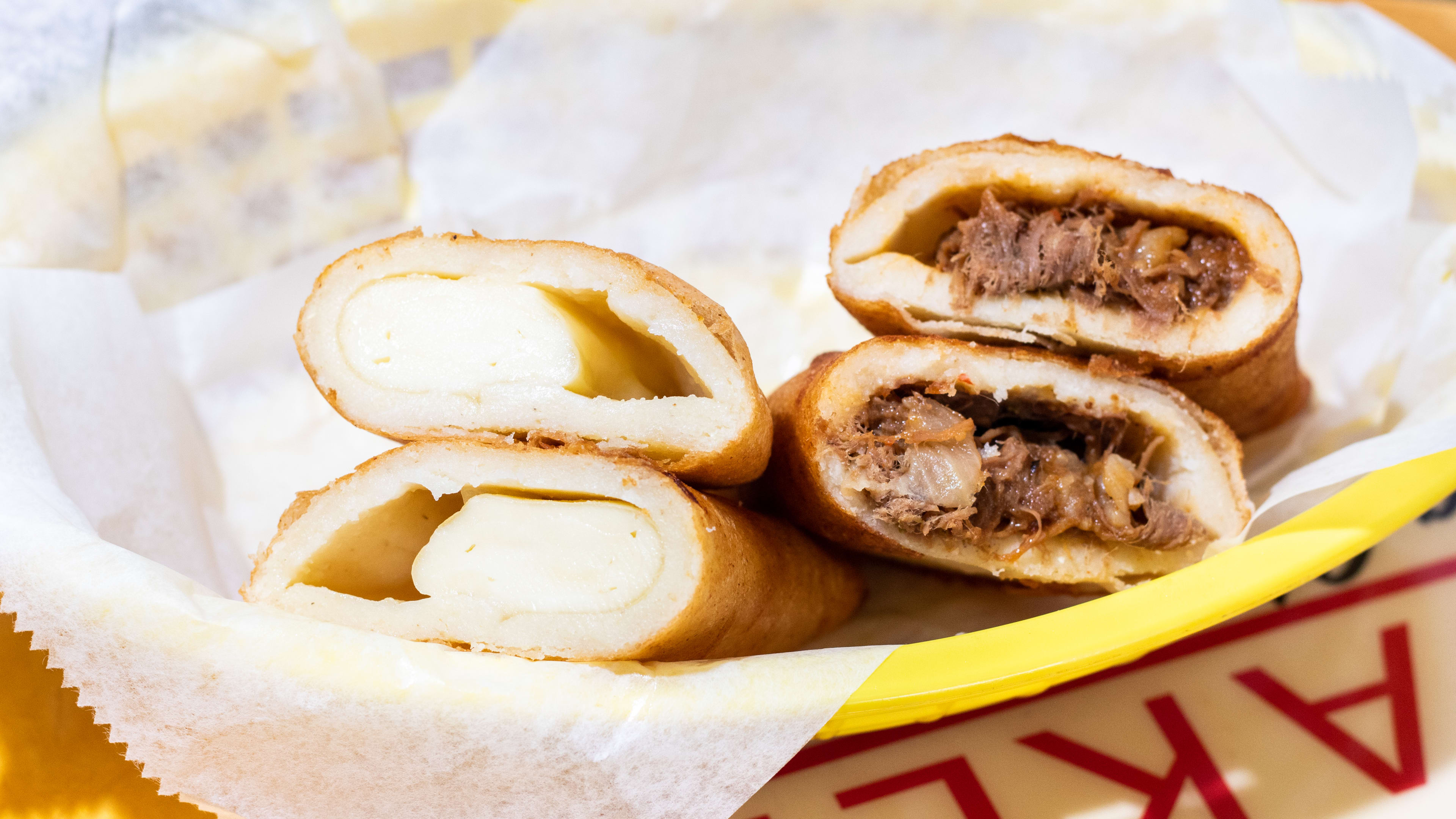 plastic basket with two empanadas cut in half to reveal cheese and meat fillings