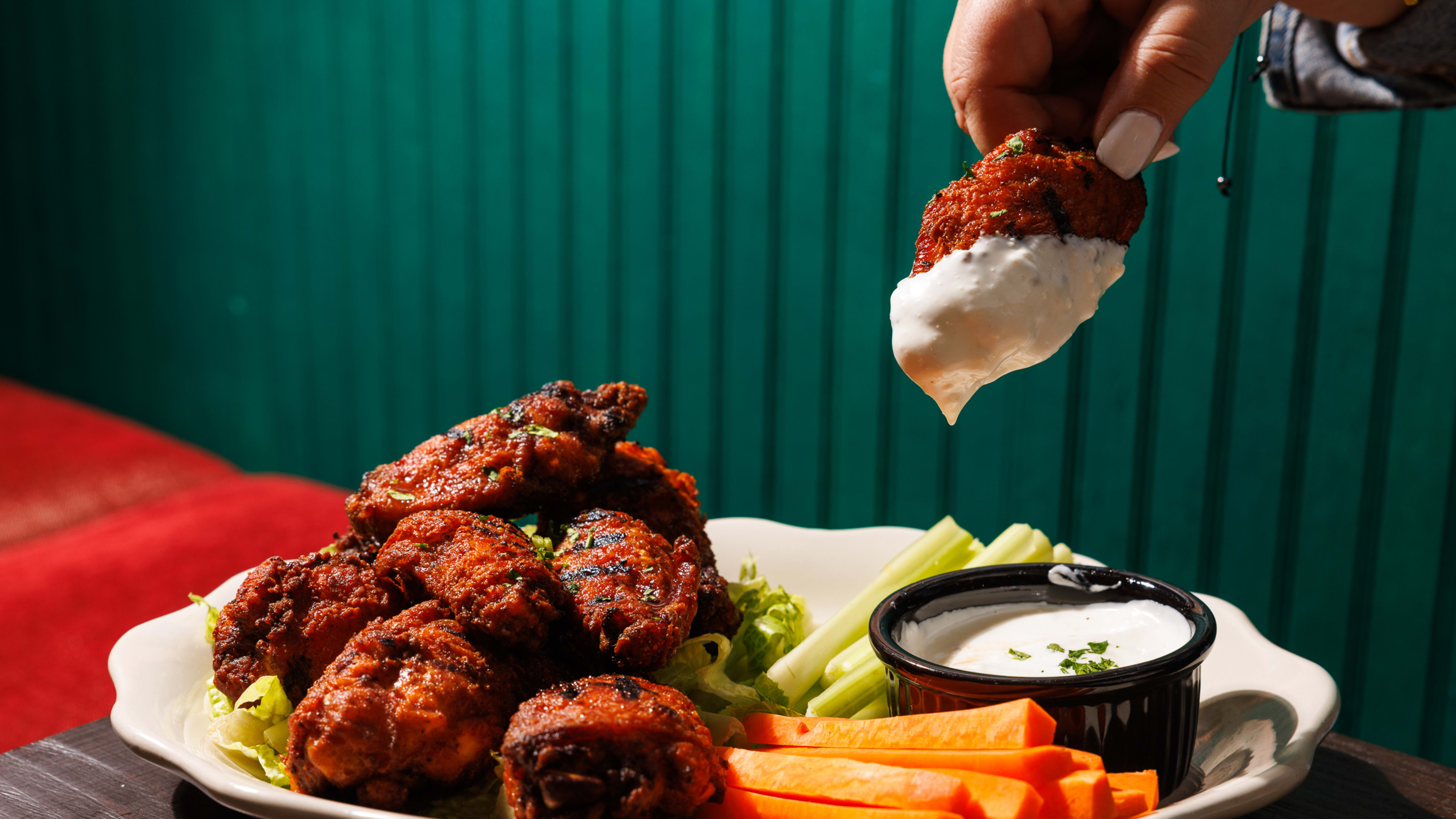 chicken wings being dipped in dressing