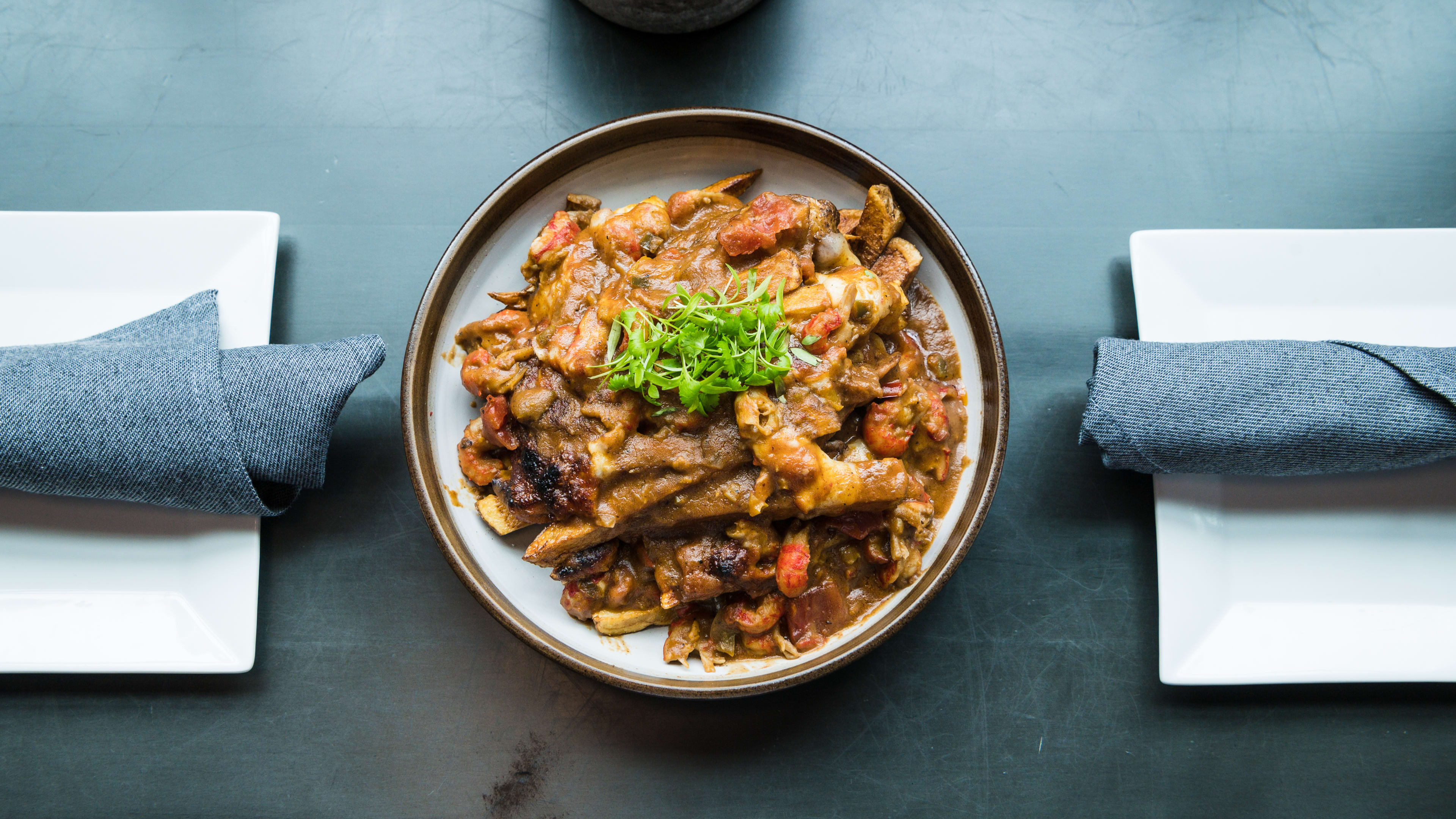 Dish of pasta on a blue table with two plates next to it.