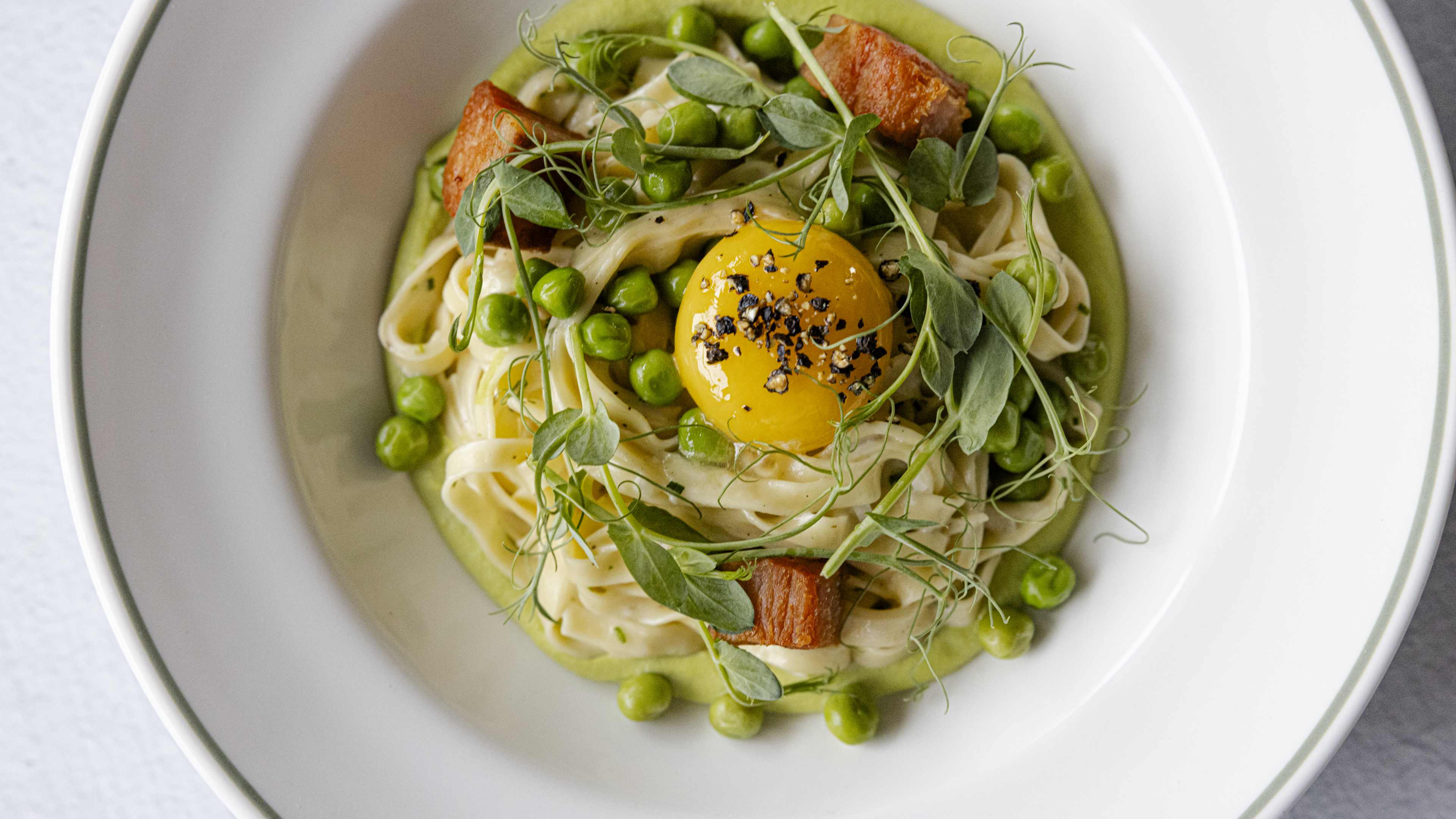 bowl of spaghetti carbonara at Bar Bludorn with green pea sauce, pea tendrils, and a raw egg yolk on top