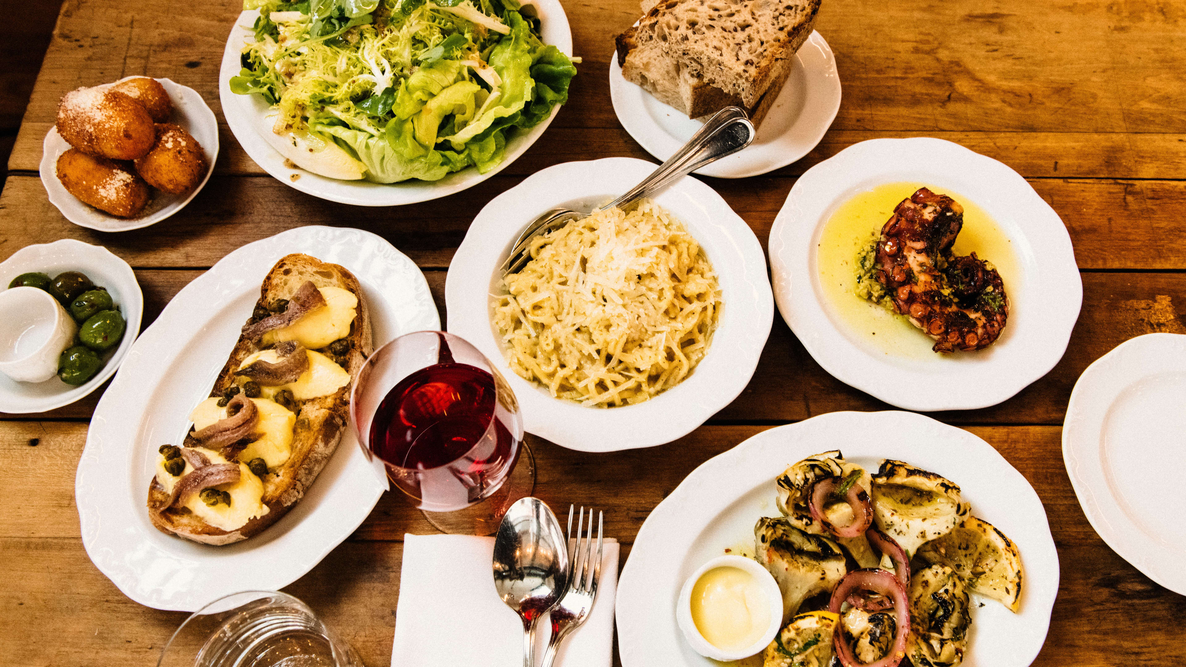 A spread of dishes, including a few pastas and a salad, on a wooden table at Via Carota in NYC