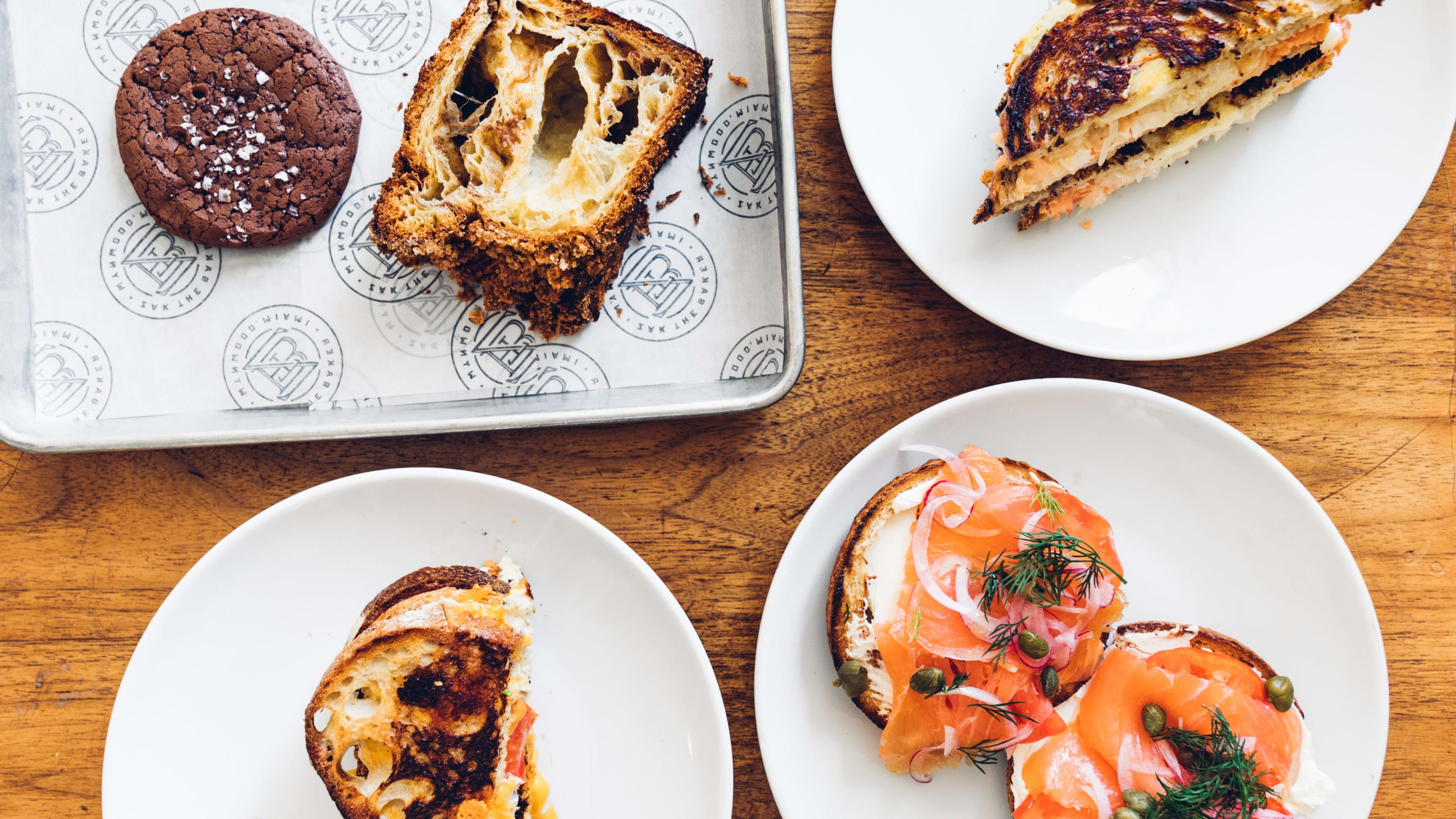 Spread of bagel with lox and capers, grilled cheese, tray with chocolate cookie and babka, and another grilled sandwich.