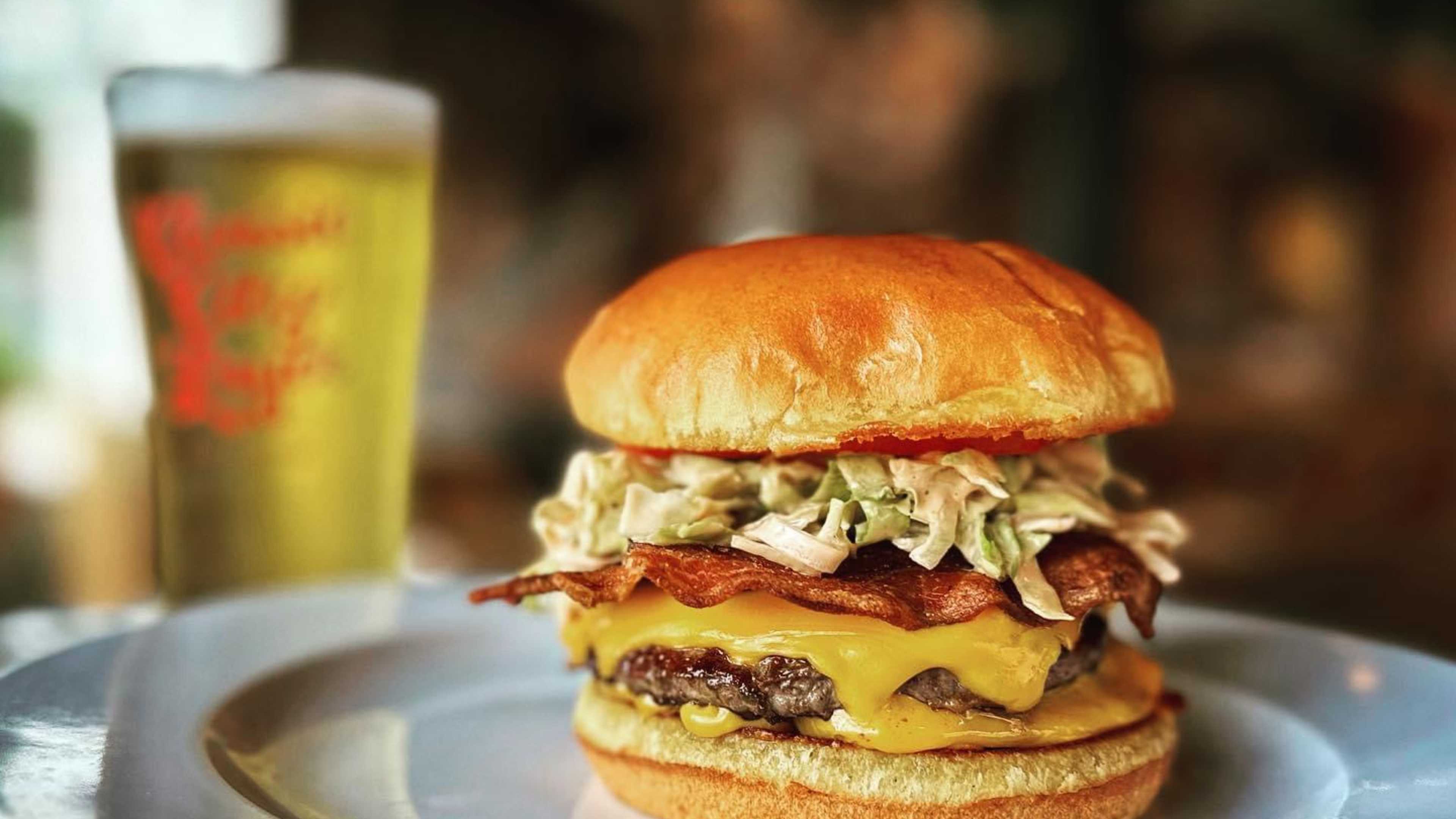 Burger with Million dressing, backon and cheese on a white plate with a beer in the background.