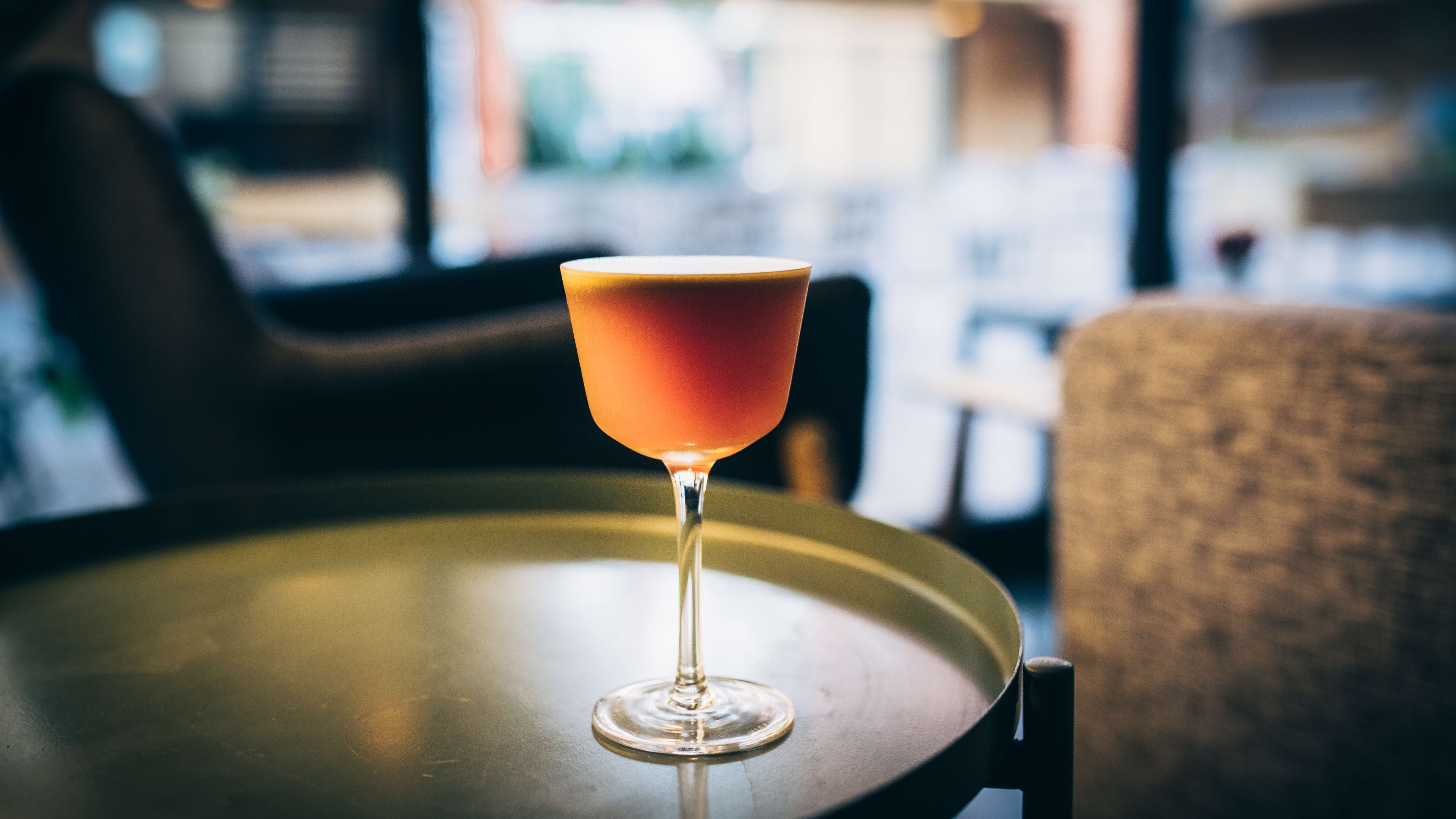 A cocktail in a fancy glass sits on a metal table.