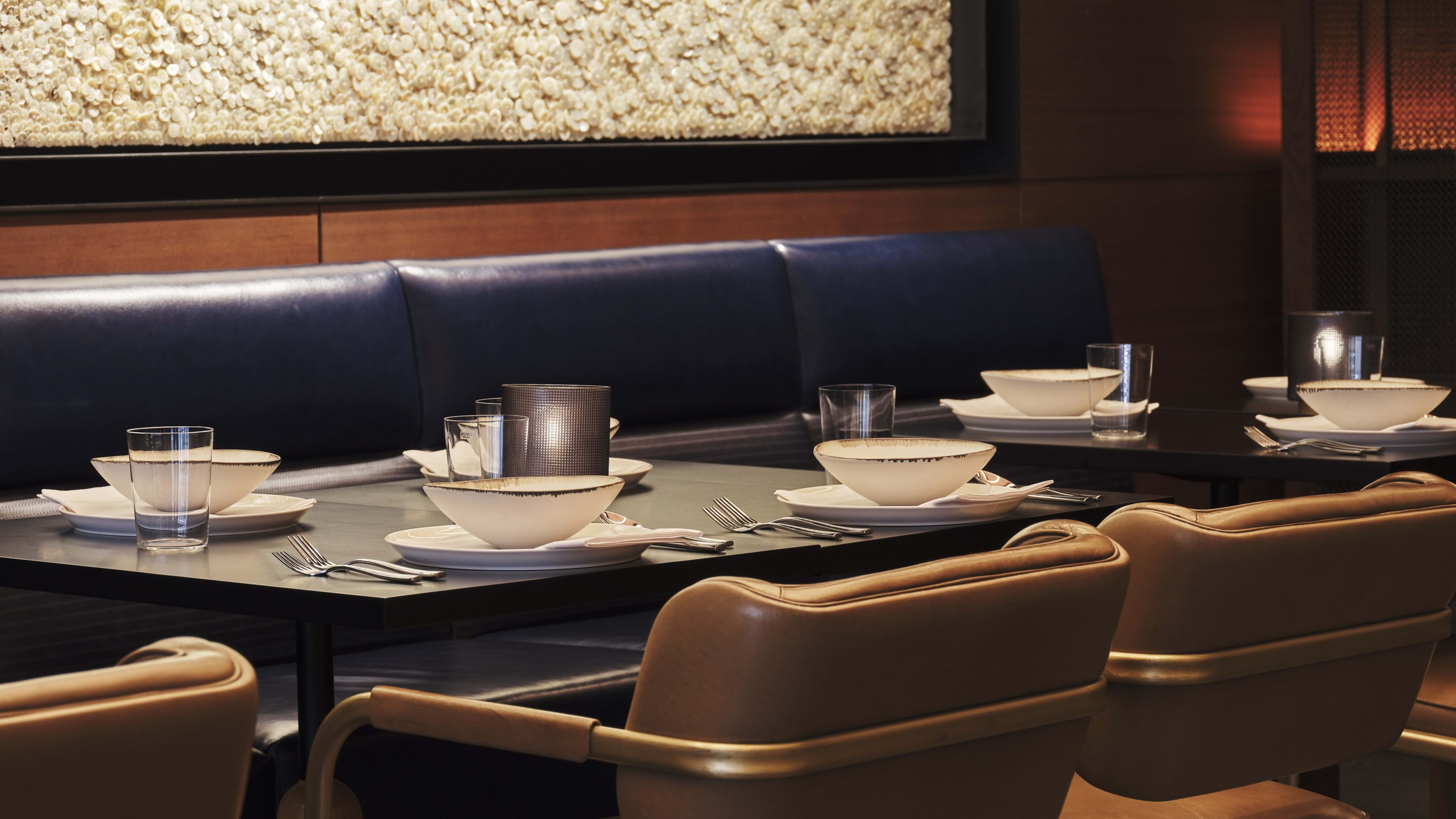 A close-up of tan leather dining chairs sitting at a table, with a blue banquette on the other side.