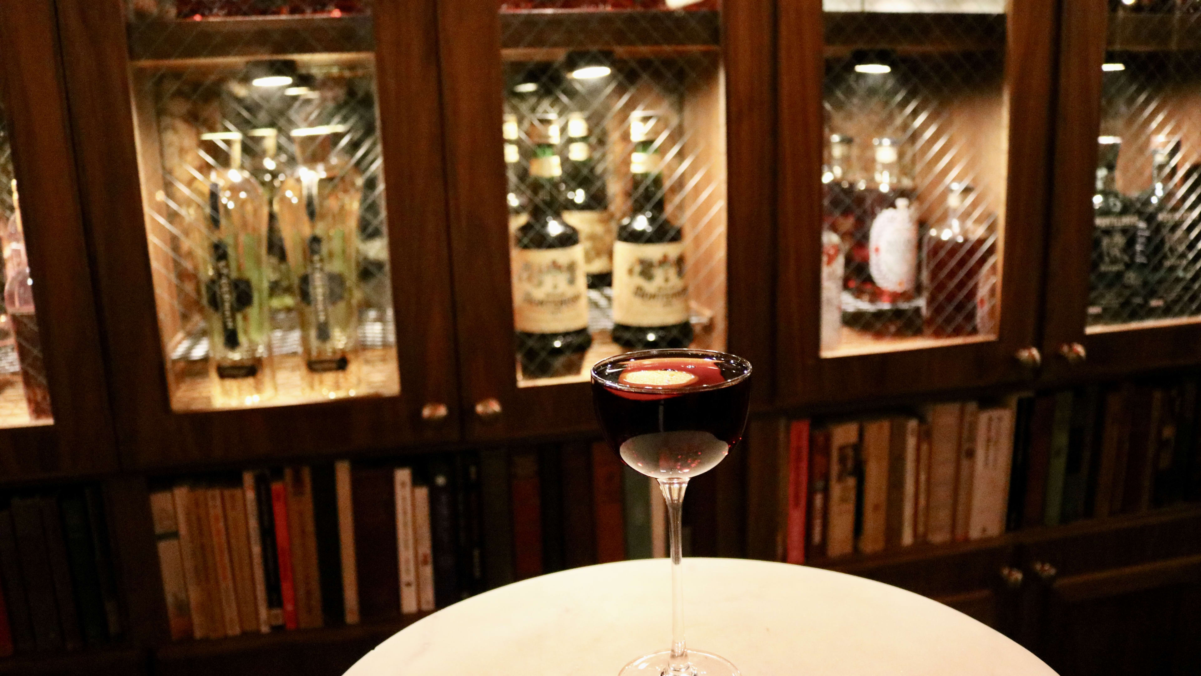 a dark cocktail in front of a wooden bar