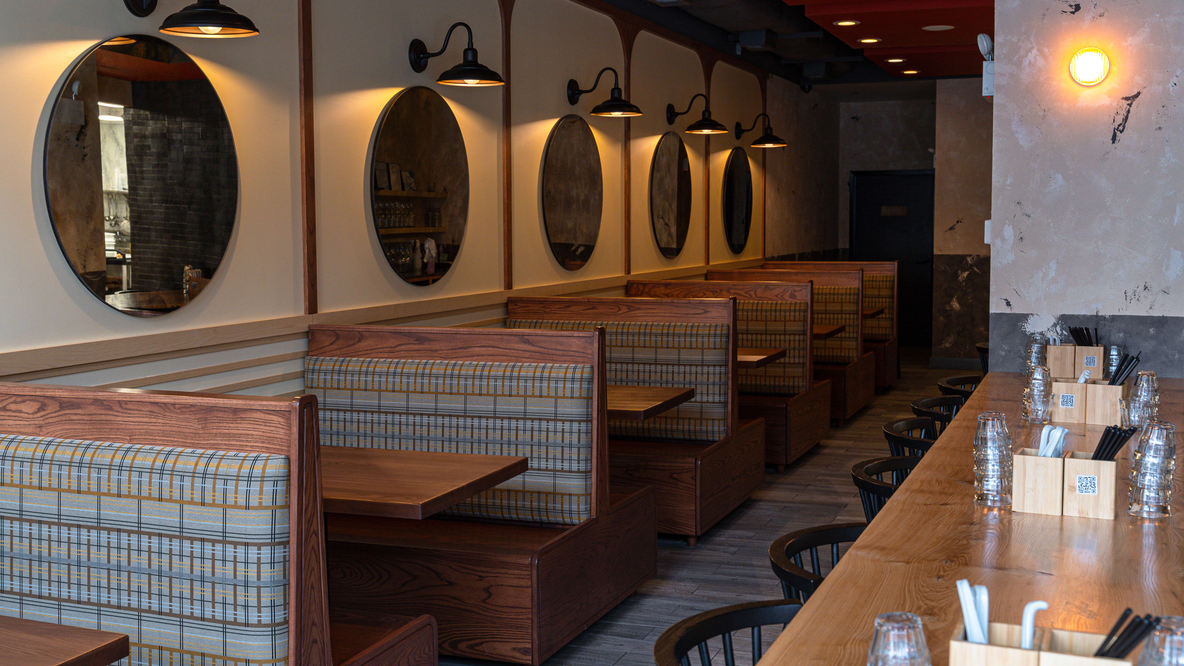 A dining room with booths, lamps, mirrors, and a communal table on the side.