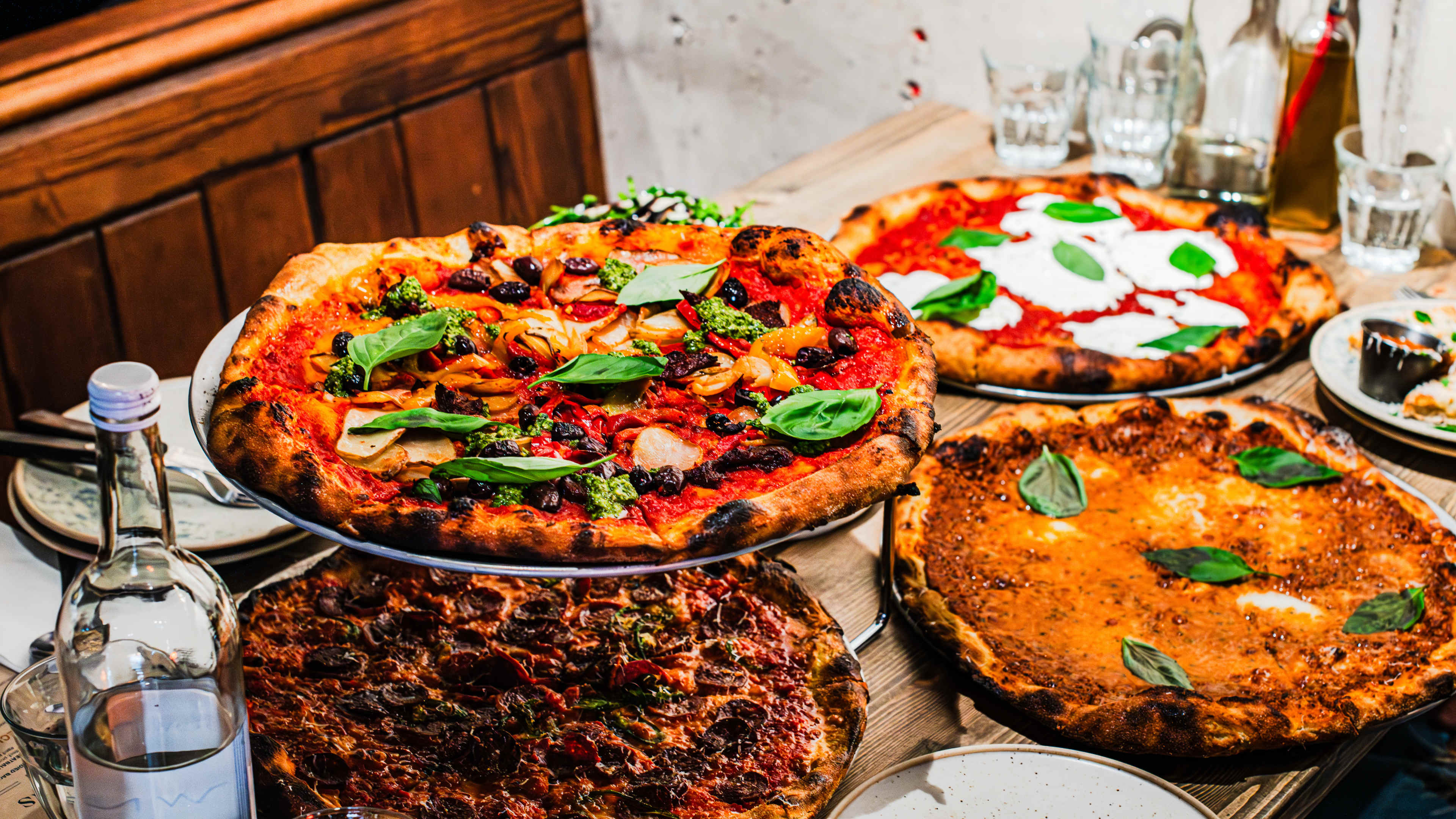 Four different pizzas from Alley Cats Pizza on a wooden booth table.