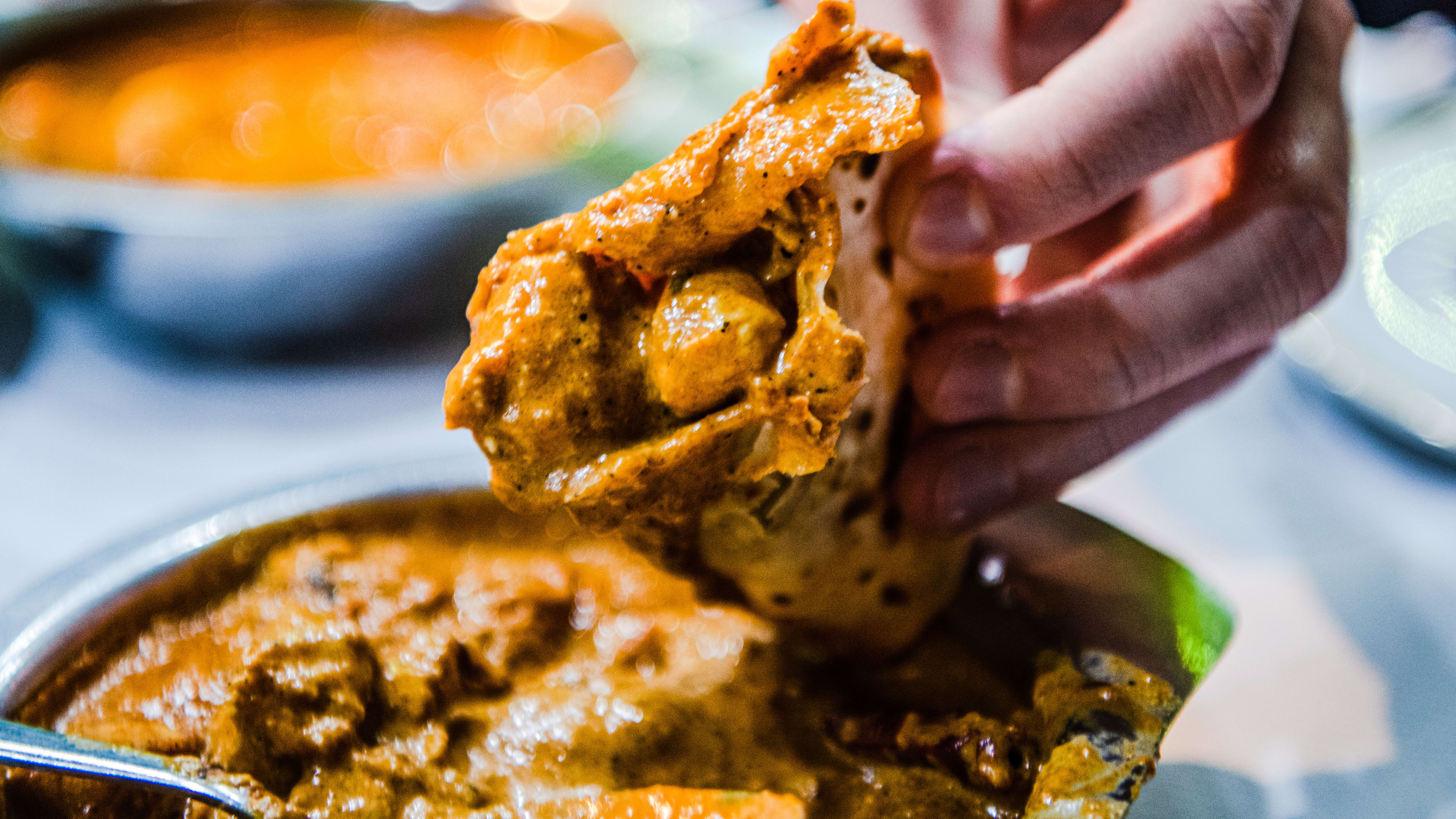 Person holding up a piece of naan that has been dipped in the ceylon chicken curry.