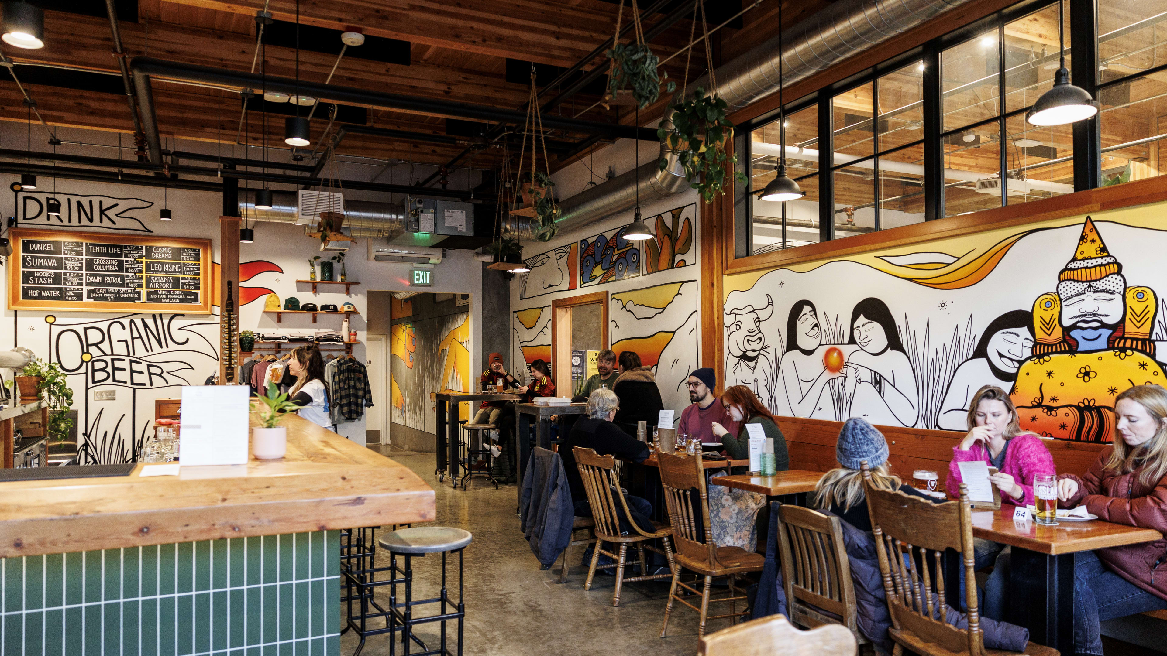 Brewery interior with colorful murals and tables close together.