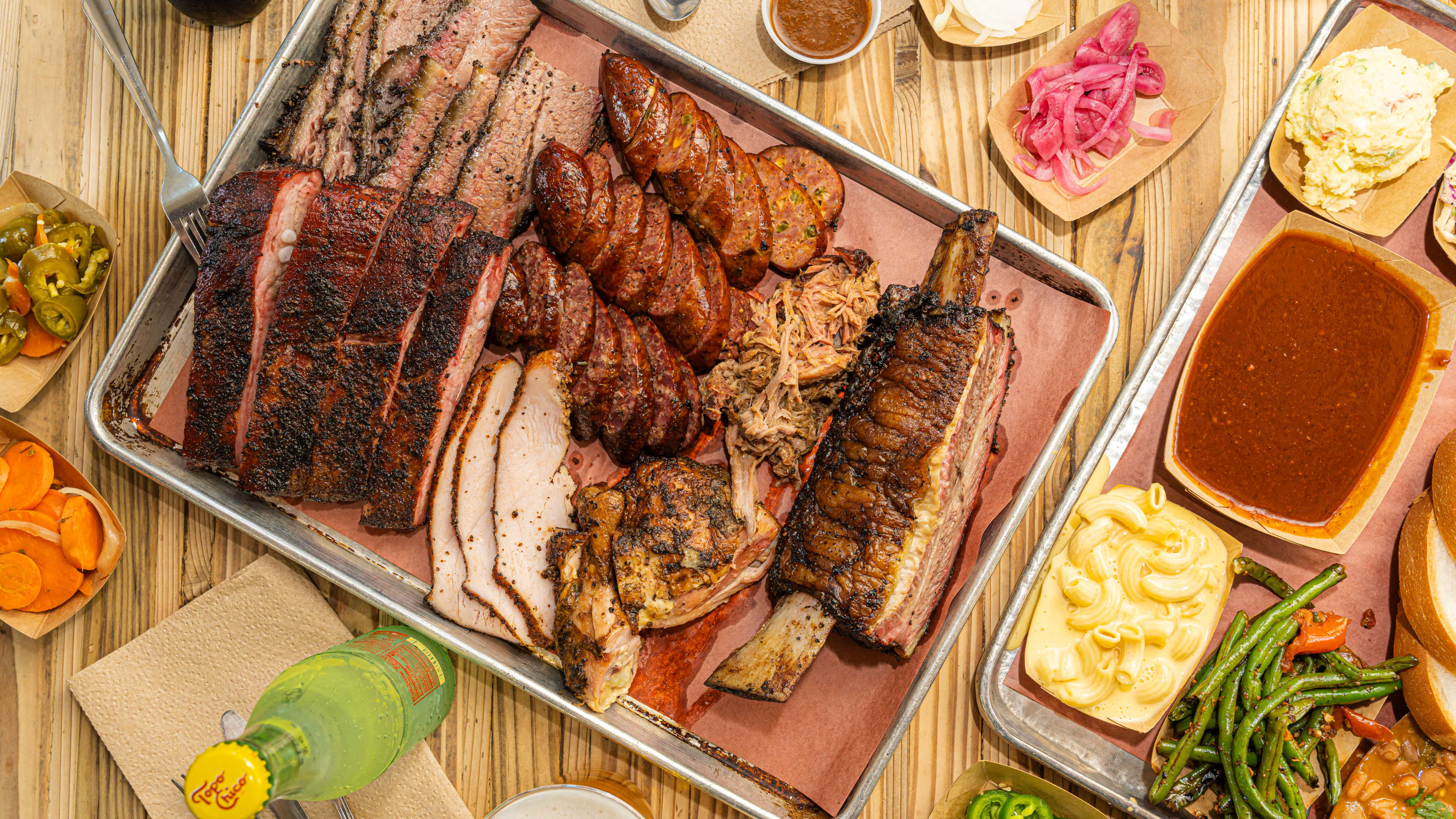 A bbq platter from The Pit Room surrounded by sides and drinks.