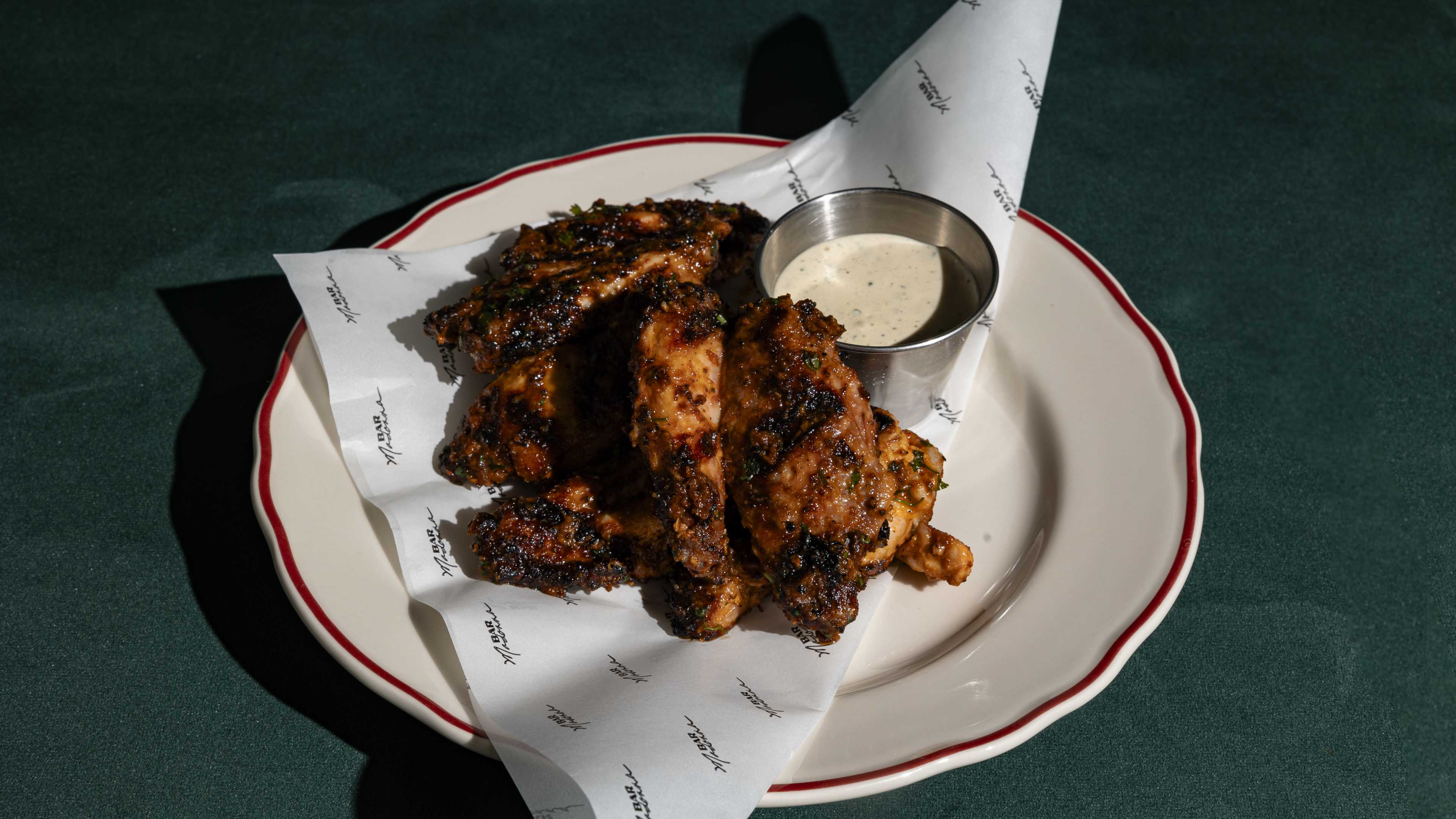 A plate of charred wings with a sauce on the side.
