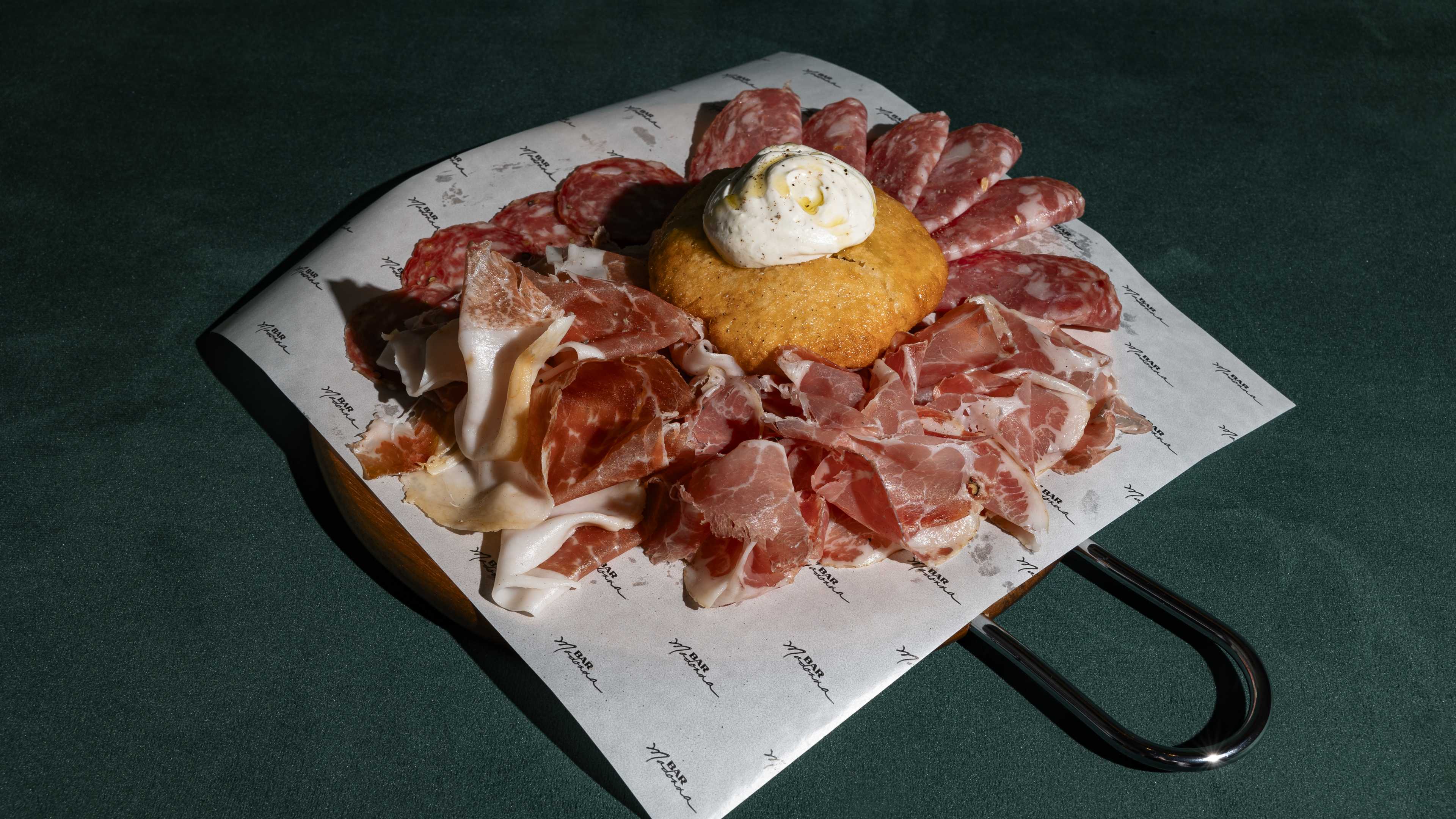 A big board covered with charcuterie, with a piece of fried bread in the middle.