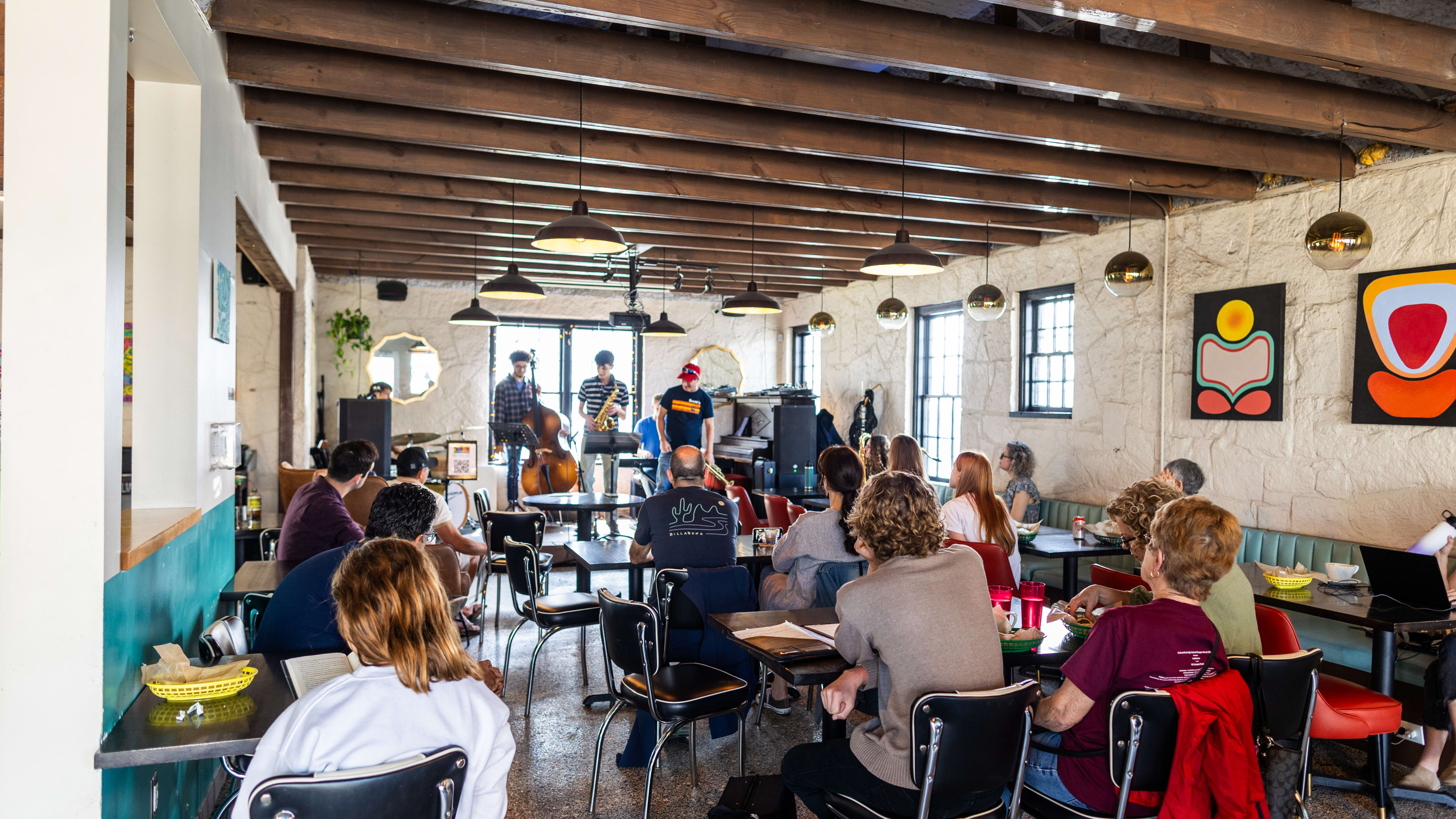 People sit at small tables inside Batch Brewing. There is abstract art on the white stone walls, wooden beams on the ceiling, and leather retro chairs.