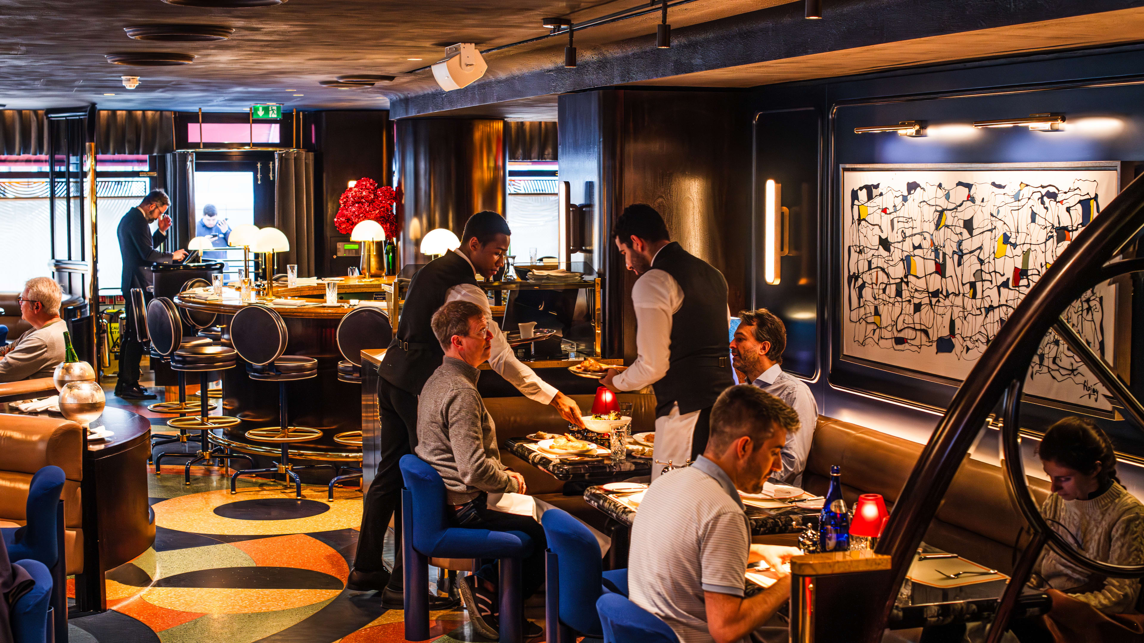 The colorful and patterned interior of Bebe Bob with patrons at tables sitting in leather booths and blue mod chairs.