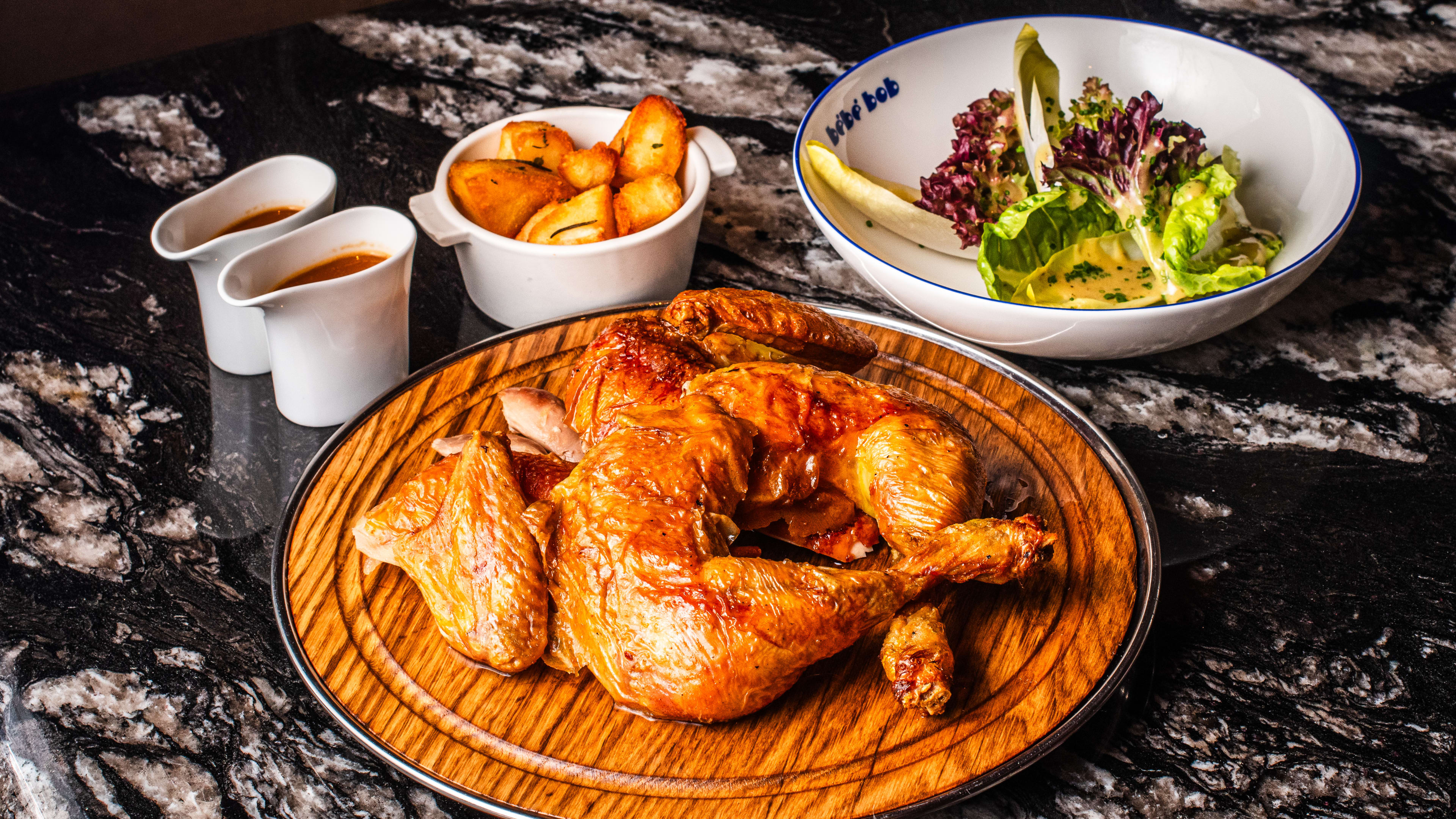 The Landes Chicken at Bebe Bob, served on a wooden plate with a side salad, roast potatoes and two sauces.