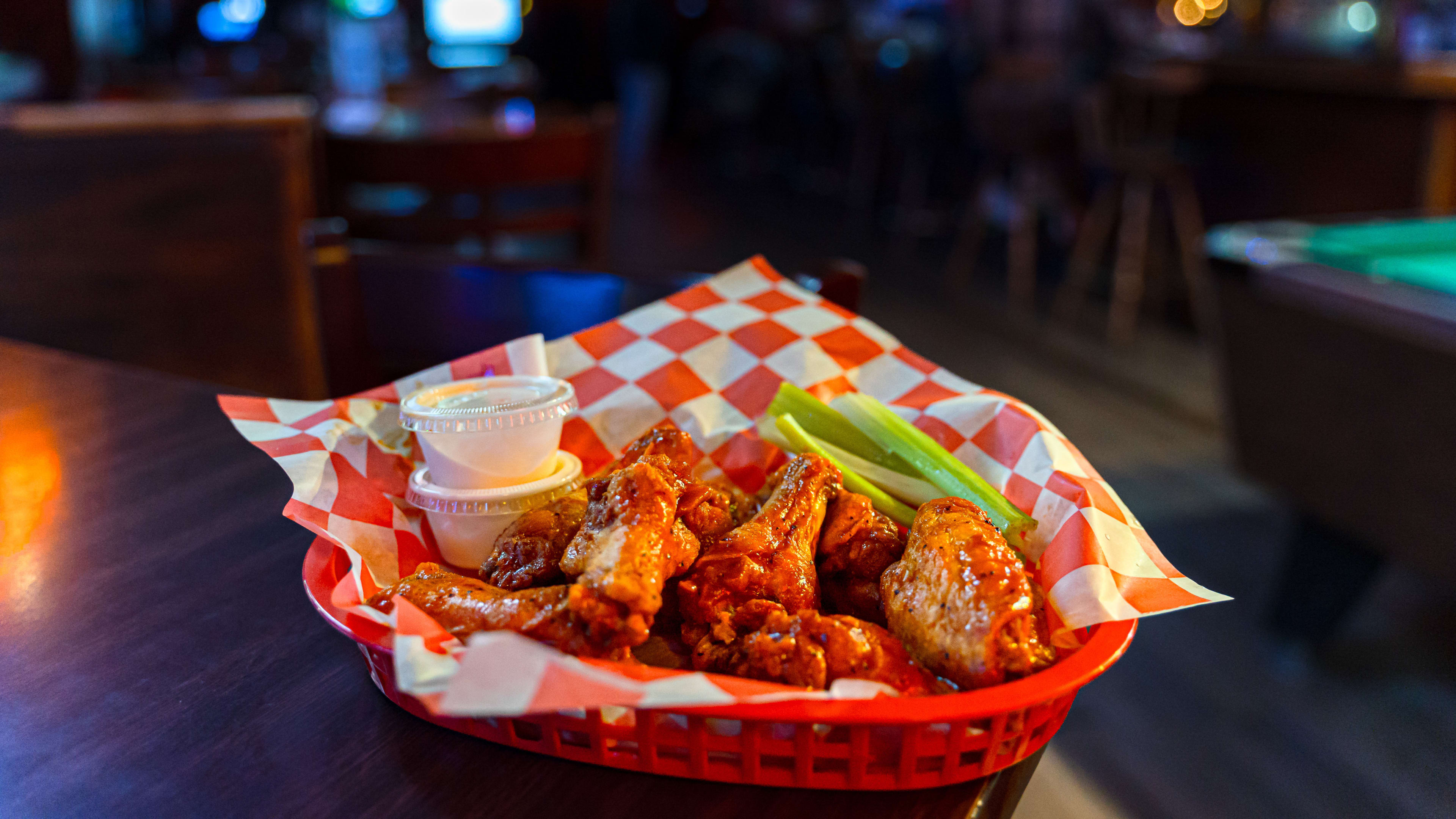 A red basket of buffalo wings with sauce and celery.